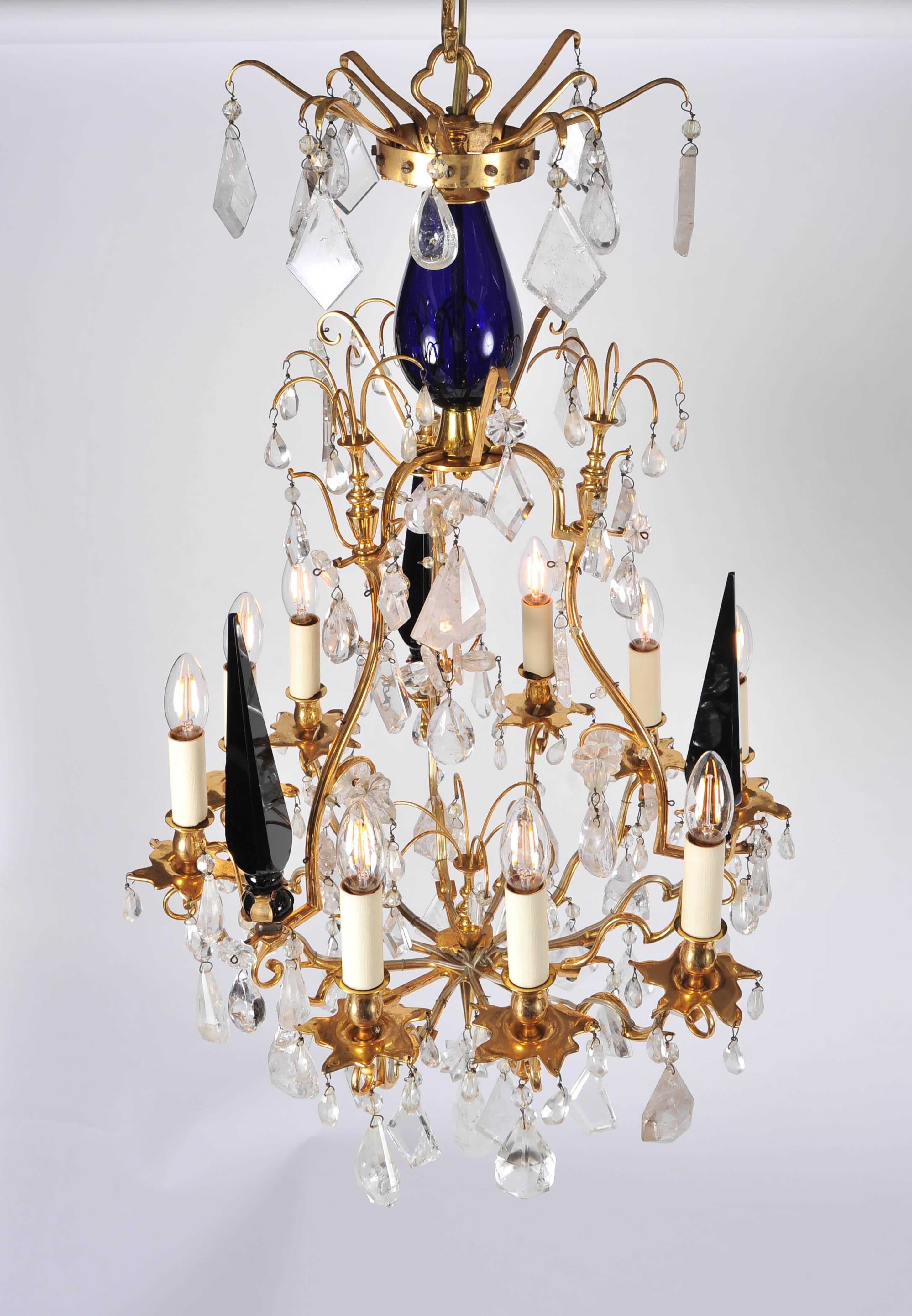 This pair of 20th century rock crystal chandeliers were formerly in residence at London's Mark's Club. The metalwork is finished in antique brass, dressed with rock crystal pear and kite pendants. Highlighted by eye catching solid blue tri-spikes