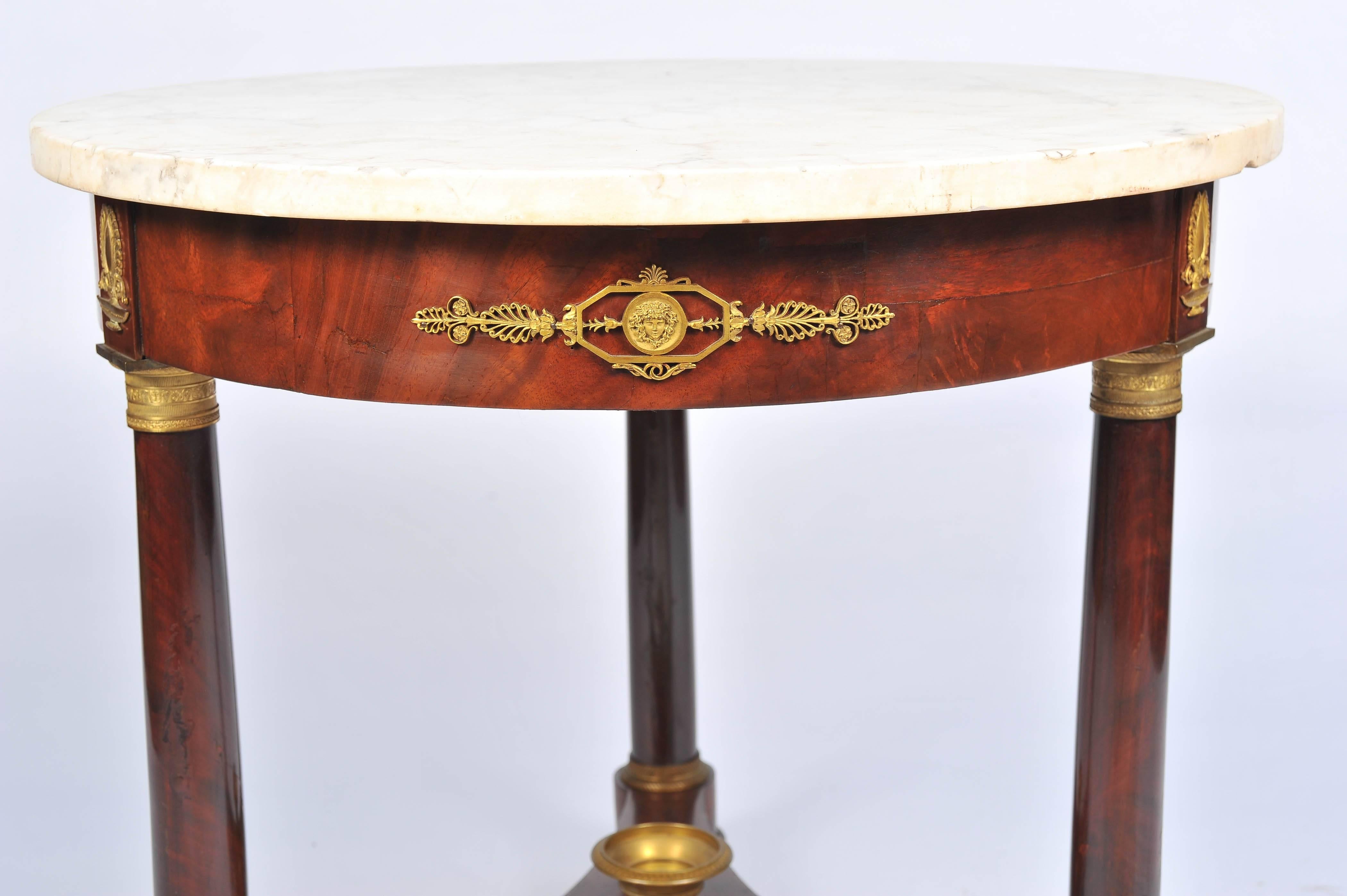 A good quality French 19th century Empire influenced Gueridon, marble topped with gilded ormolu-mounted, mahogany veneered, raised on three round turned legs, united by a triform stretched with an urn in the middle and raised on castors.