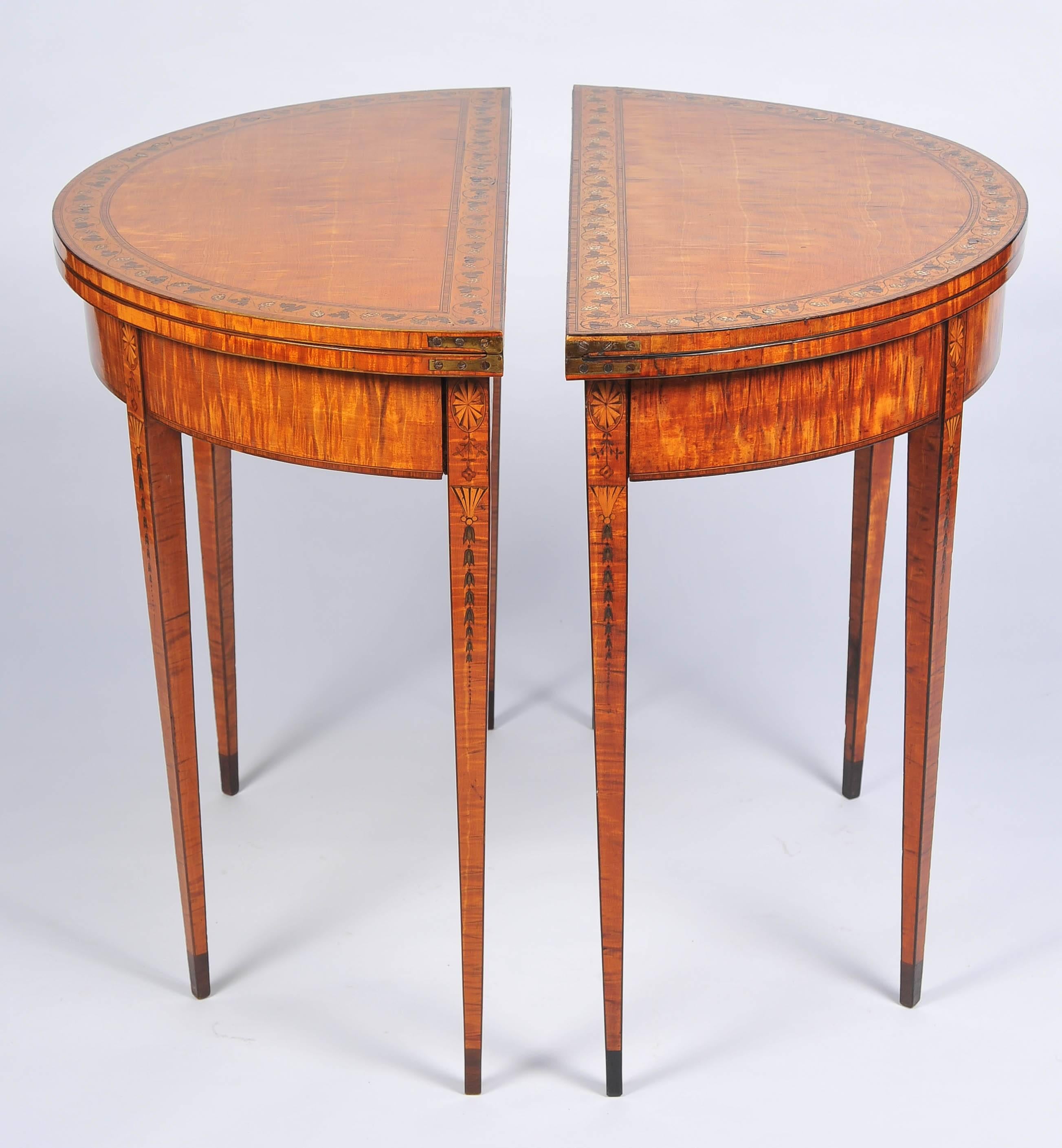 A fine quality pair of Sheraton period satinwood demilune card tables, having crossbanding to the tops of vine leaves and grapes, raised on square tapering legs, inlaid with shell and leaves, terminating in ebony veneered feet.
 