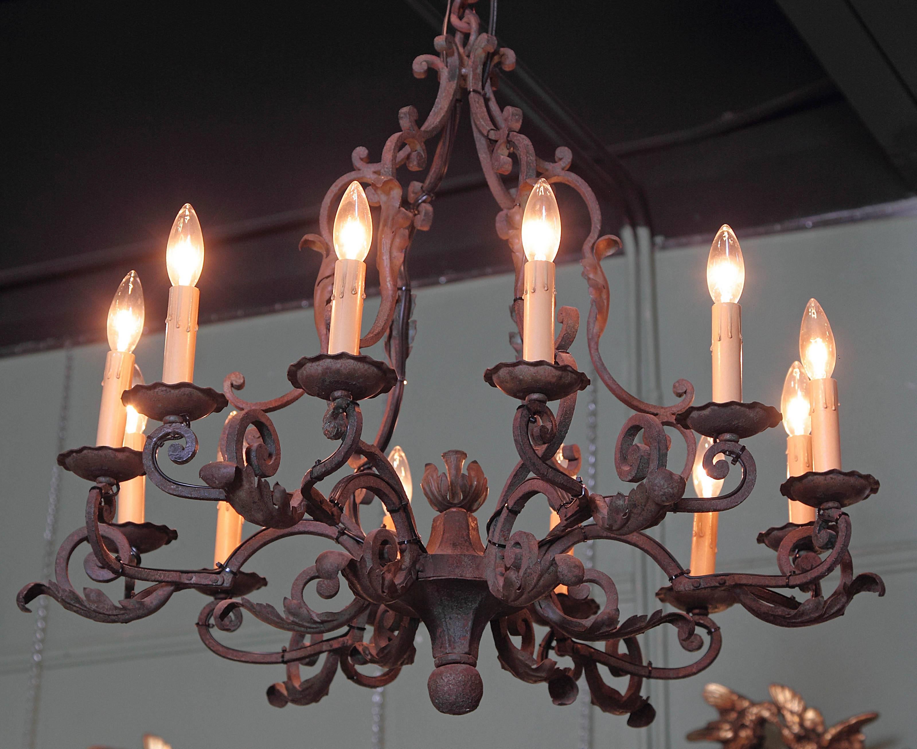 This elegant, antique chandelier was created in France, circa 1900. The round, iron light fixture features ten scrolled arms with light, decorative, high relief leaves, and a center floral finial at the base. The fixture has new wiring for easy use