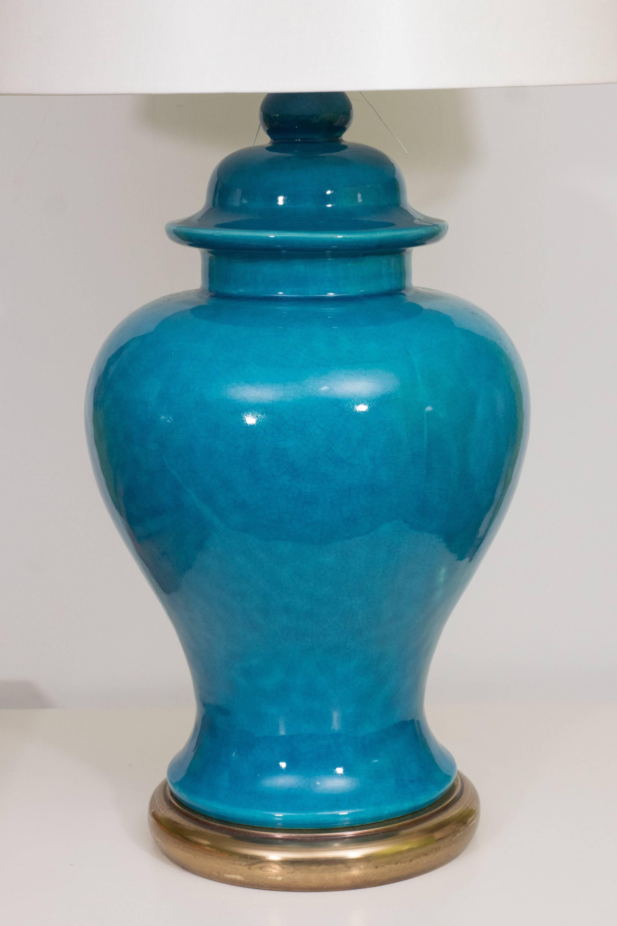 A stunning pair of ceramic urn lamps in a beautiful shade of blue on a brass base with cream colored drum shade.