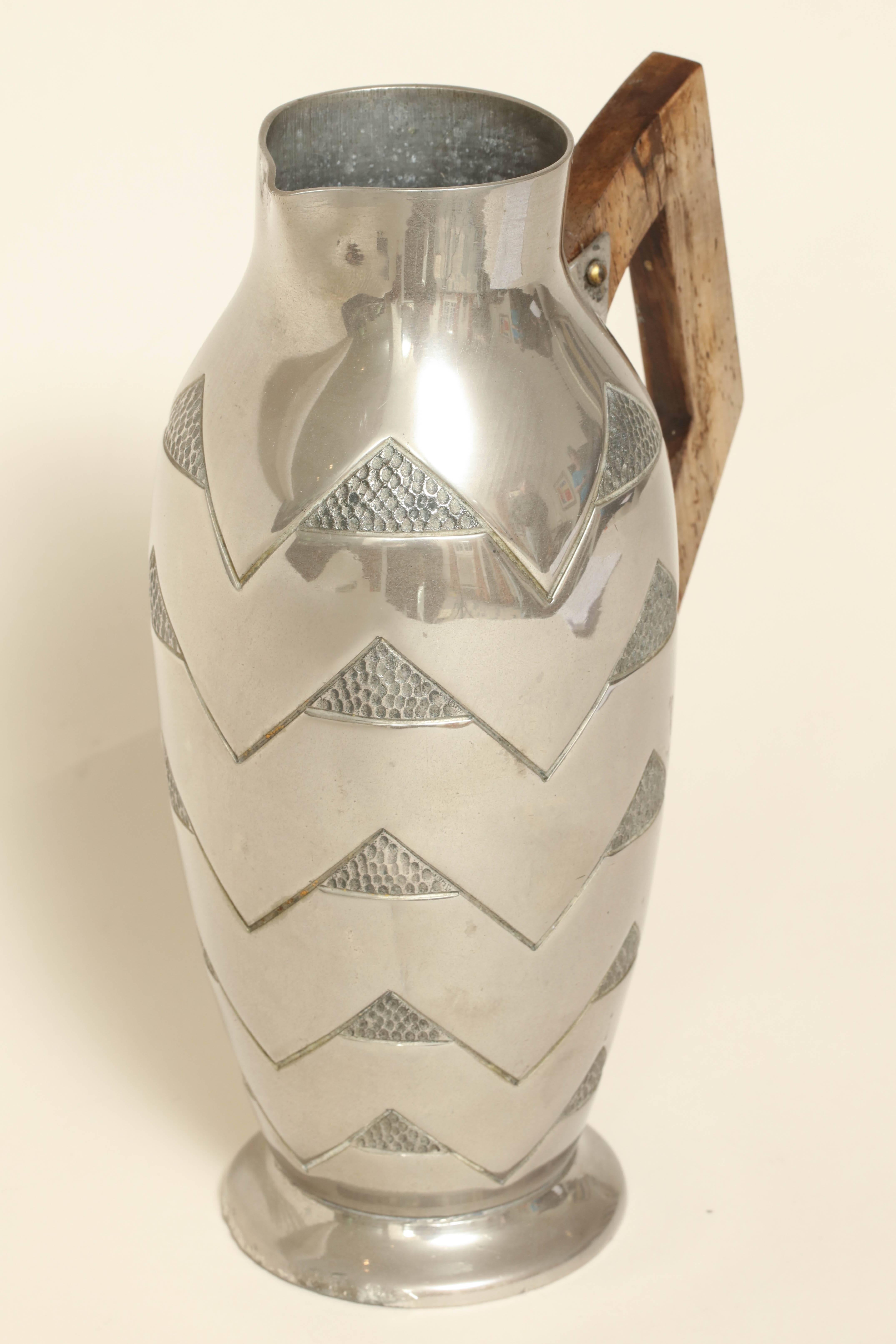 Measures: 8 7/8'' high; 5'' wide; 3 ½'' long

Hand-wrought dinanderie pewter pitcher in the mountain pattern with an angled wood handle.

Signed R. Delavan on the side/ impressed LES ETAINS/ R D underneath.