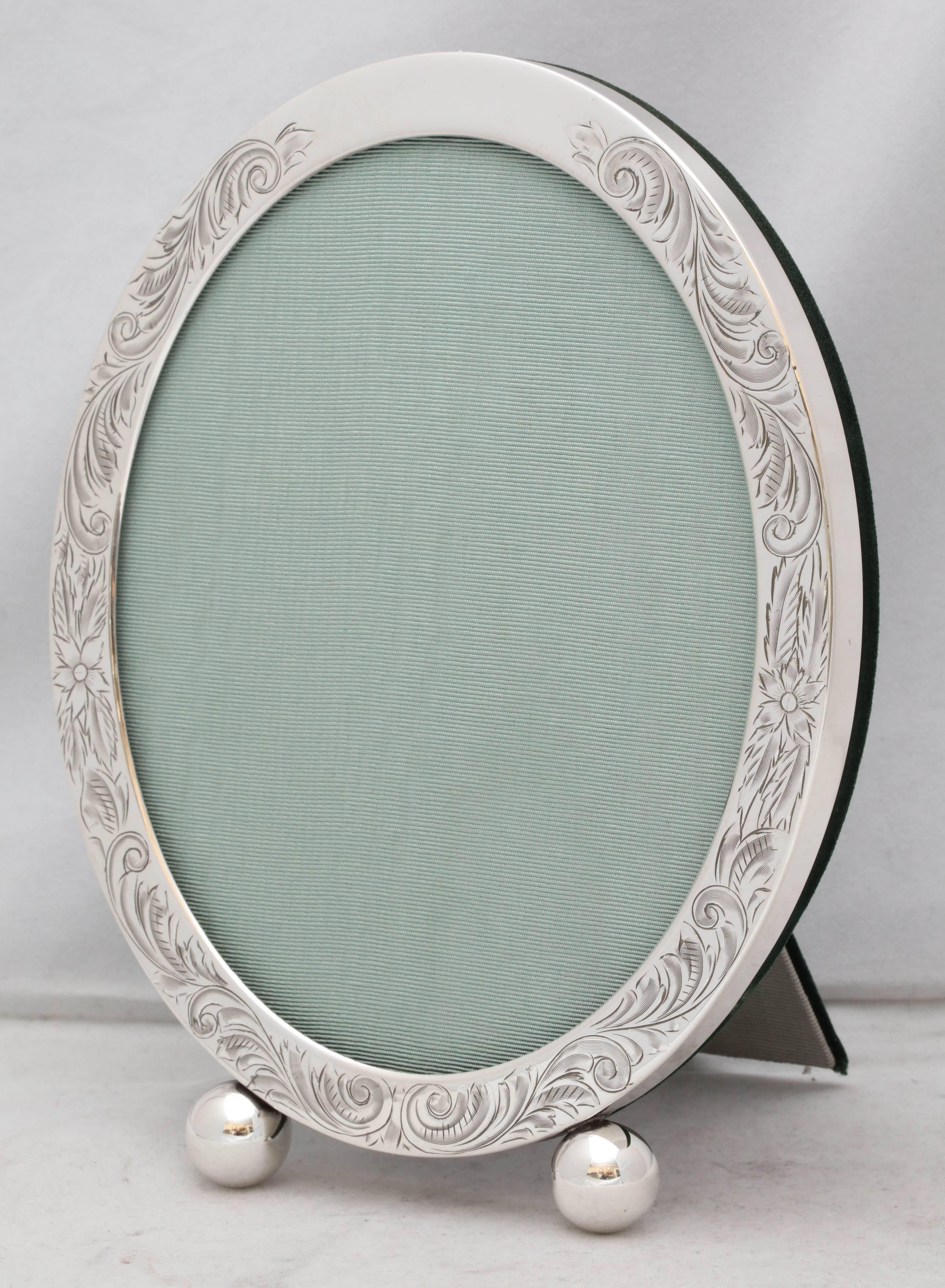 Edwardian, sterling silver, etched oval picture frame on ball feet, Unger Brothers Co., New Jersey, circa 1905. Lovely etched design. Has original convex glass. Measures: 8 inches high x 6 inches wide (at widest point) x 4 inches deep when easel is
