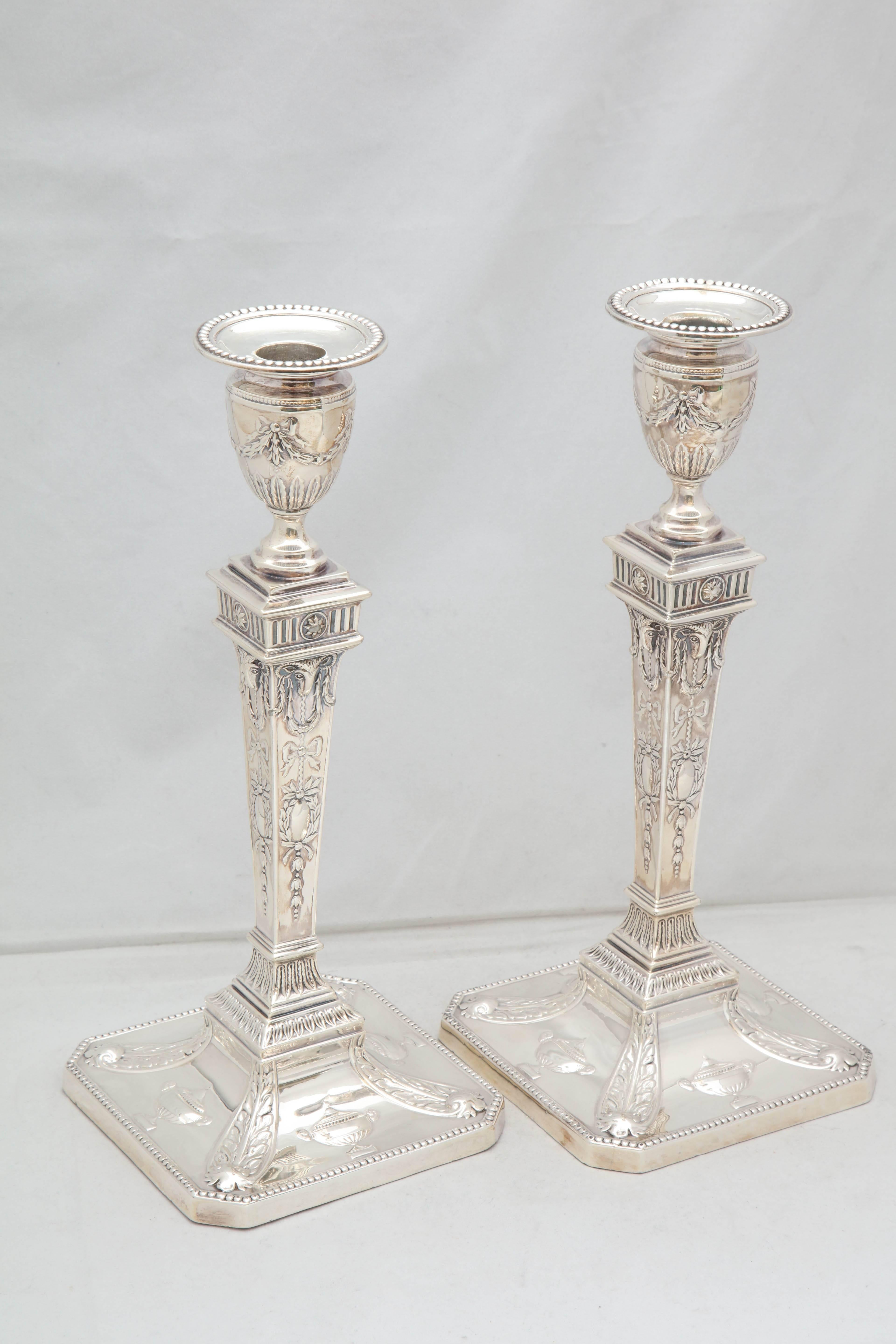 Tall pair of Edwardian, sterling silver, Adam Style candlesticks, London, 1904, Charles Boynton & Sons, Ltd.- makers. Measures: 12 inches high x 6 inches wide x 6 inches deep. Square, bases. Weighted. Decorated with garlands, ram's heads, urns, etc.