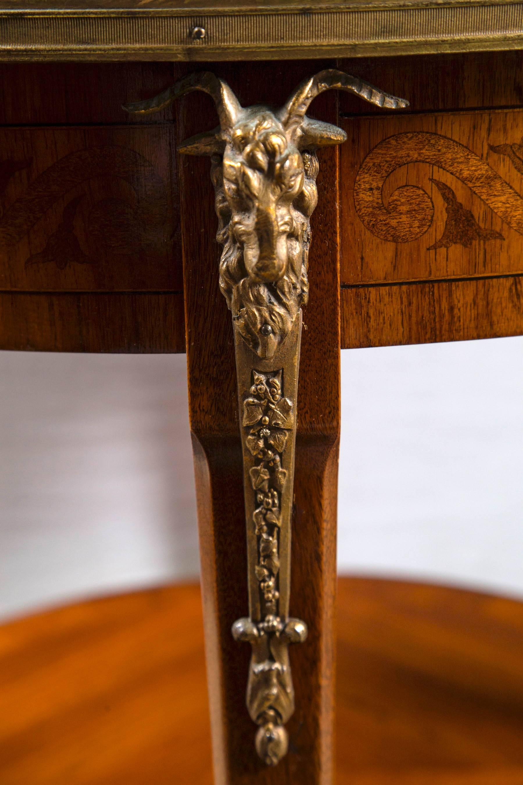 A wide border of marquetry wood surrounds the marble which is set slightly below. Matched veneered lower shelf. Marquetry appears to be satin wood, mahogany and sycamore, in a floral garland pattern. Bronze mounts with rams heads. Brass edging to