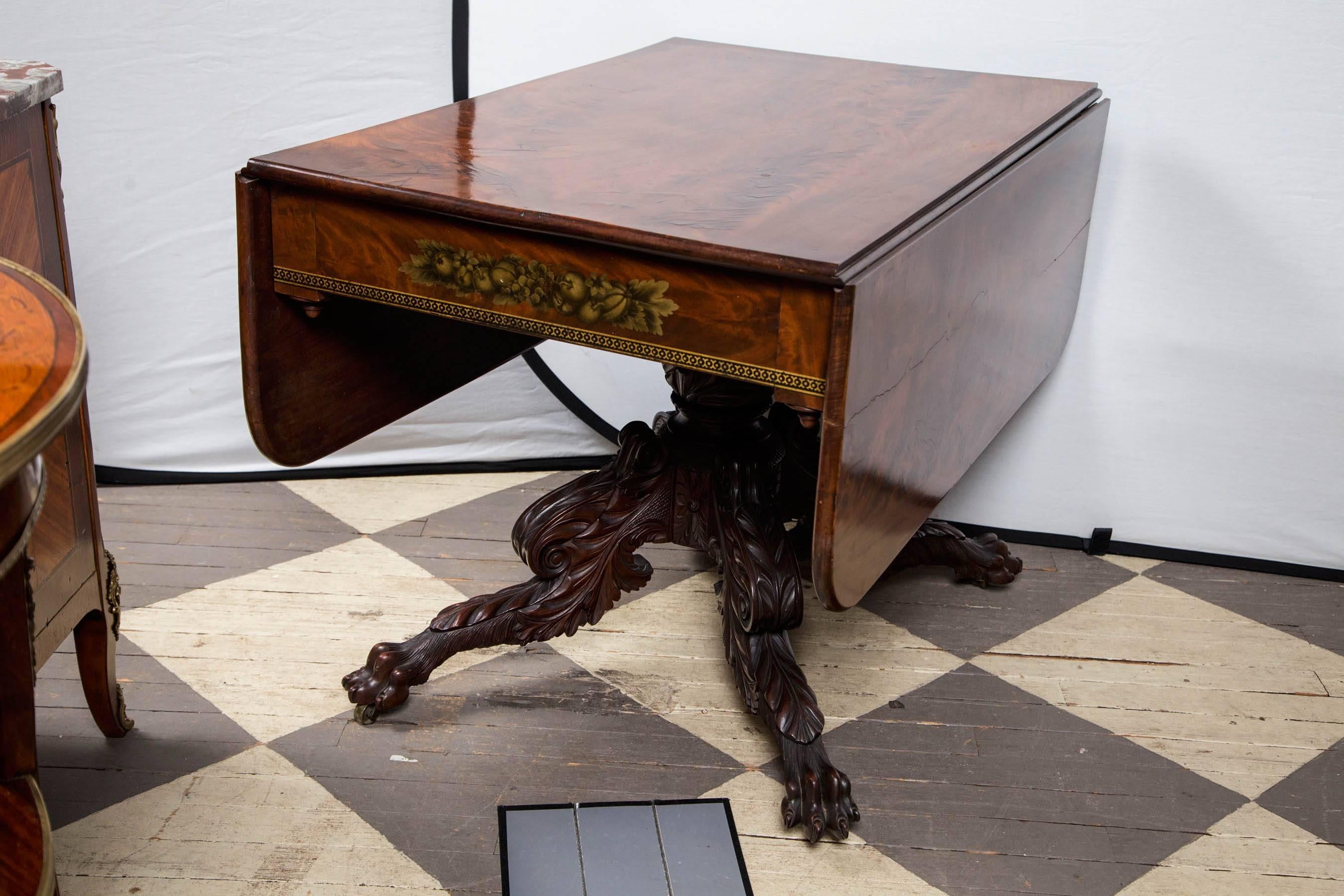 Flame mahogany single board top and drop leaves. Original stenciling of fruit and leaves with a classical band below. Crisply carved center pedestal with carved acanthus leaves and four legs with acanthus leaf and paw deep craving. Original