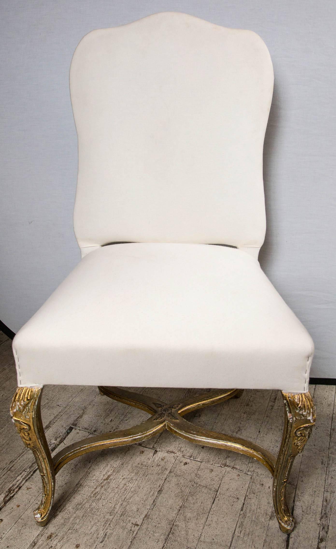 This set is fully upholstered in muslin, and ready for your fabric. There are two armchairs and eight side chairs. A thin gilt finish over some visible older paint. Flaking to the surfaces. Serpentine top crest, cabriole legs and x form