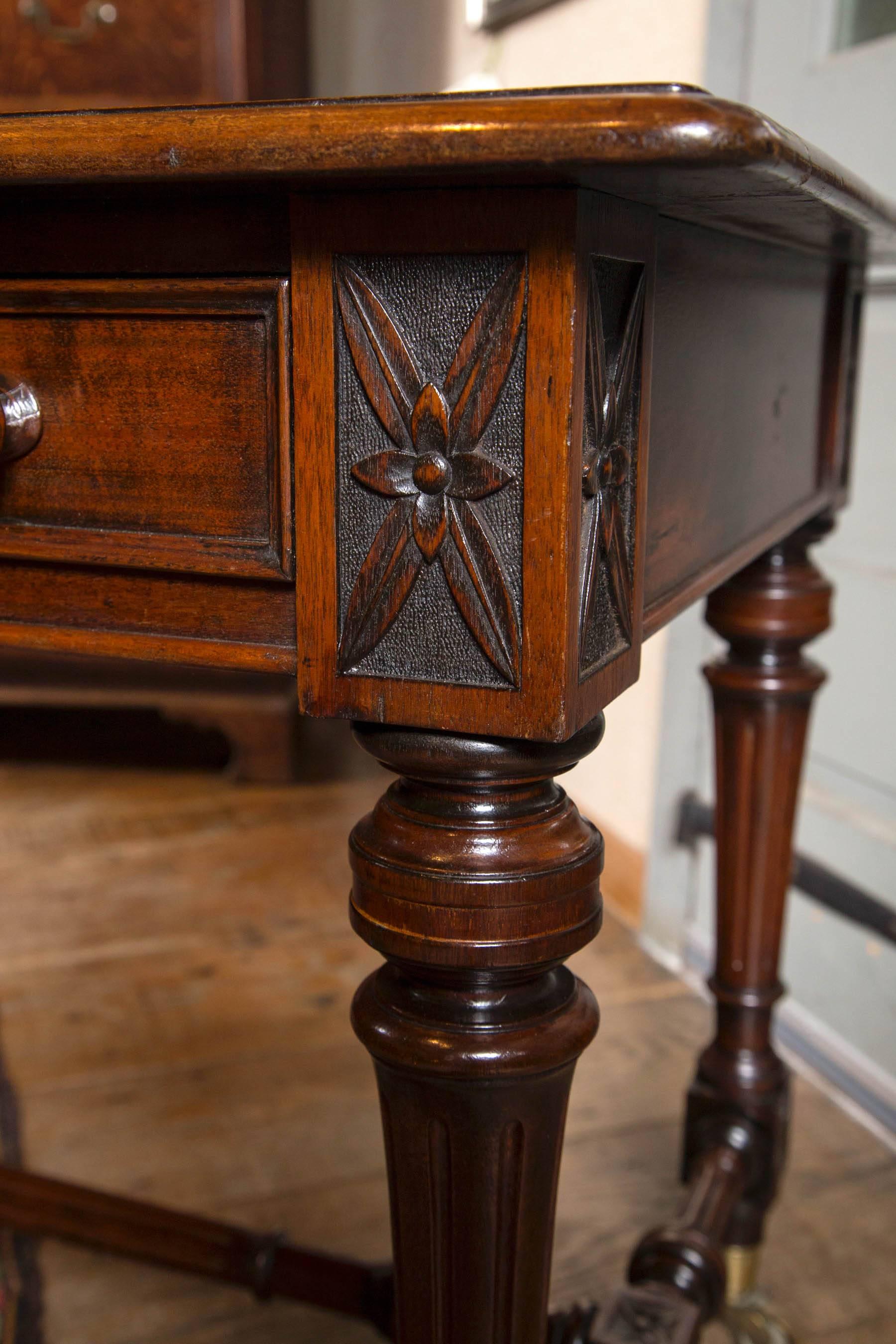 Victorian library table / desk features three drawers with original wood knob and turned and fluted legs ending in carved floral block feet resting on brass casters. Turned H stretcher also with carved floral blocks add unique look to this handsome