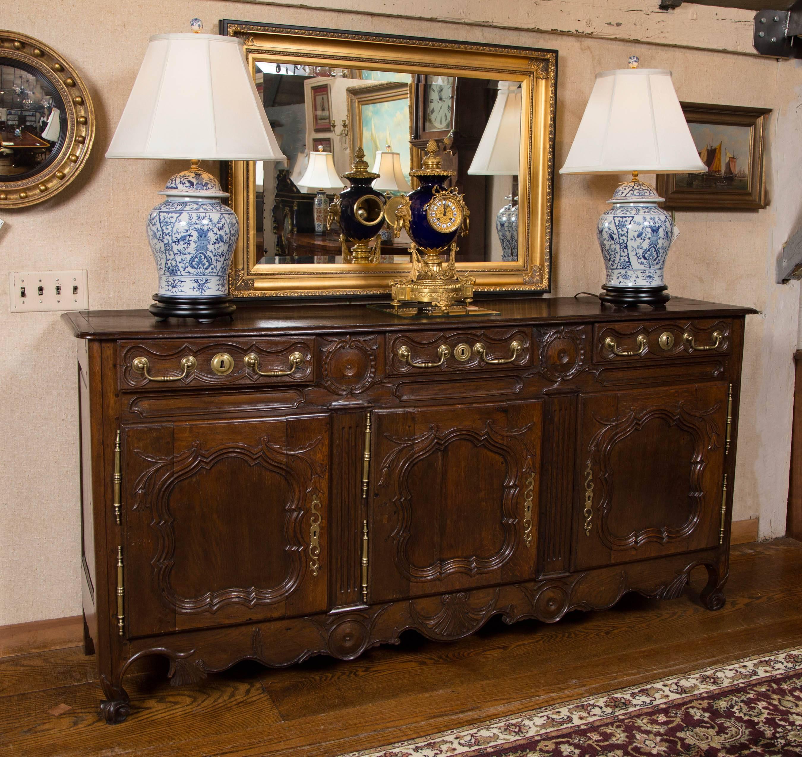 French oak enfilade with three-plank top, breadboard ends and thumb moulded edge over three drawers and three paneled doors. Robust carved doors separated by garland wreaths sitting atop fluted columns resting on circular medallions. Shaped and