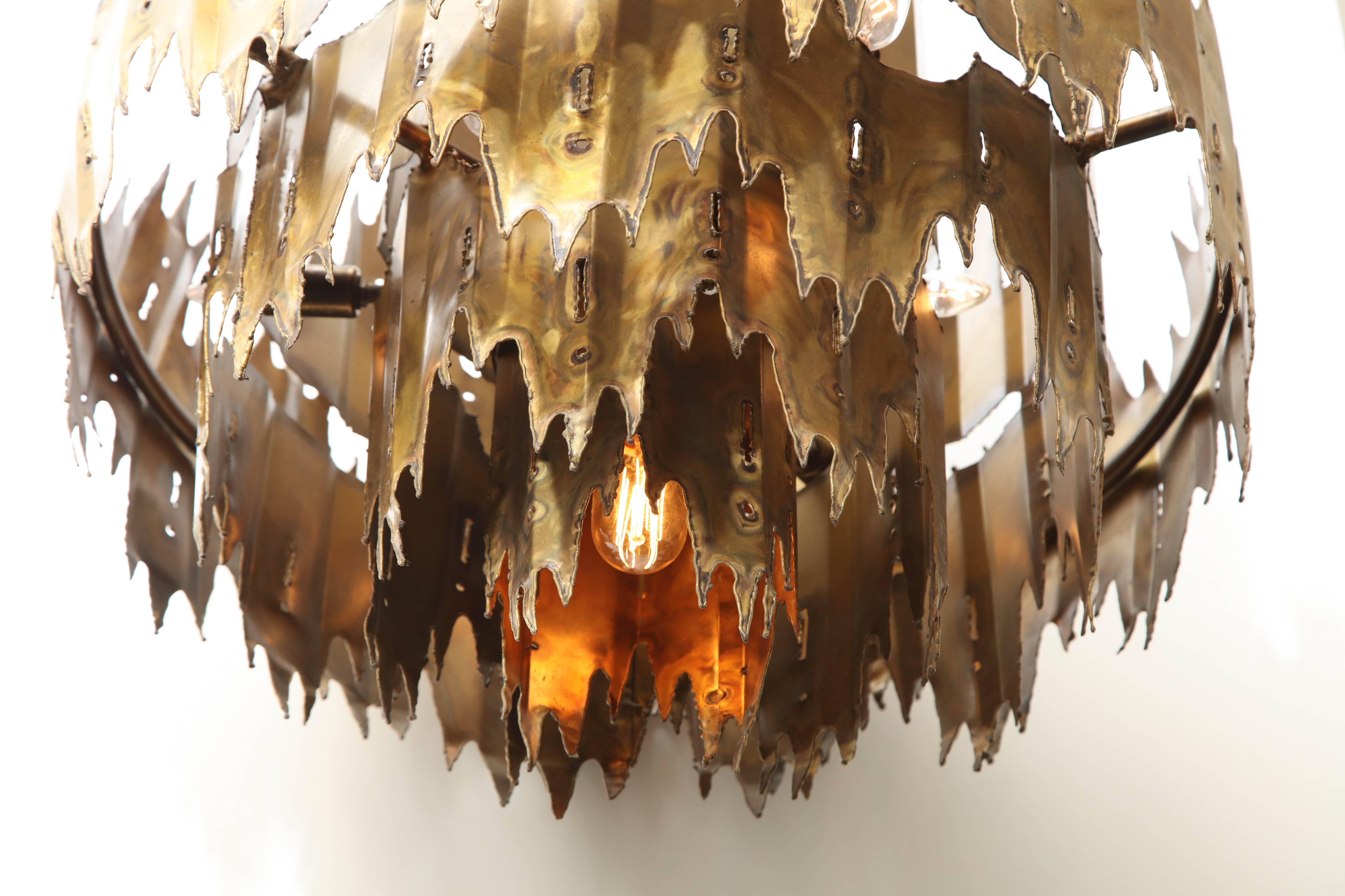 A large torch cut brass chandelier designed by Tom Greene for the Feldman Lighting Company of Los Angeles, circa 1960. Originally starting with his own dental lab and making jewelry as a hobby, Tom Greene gradually began to work on larger pieces in