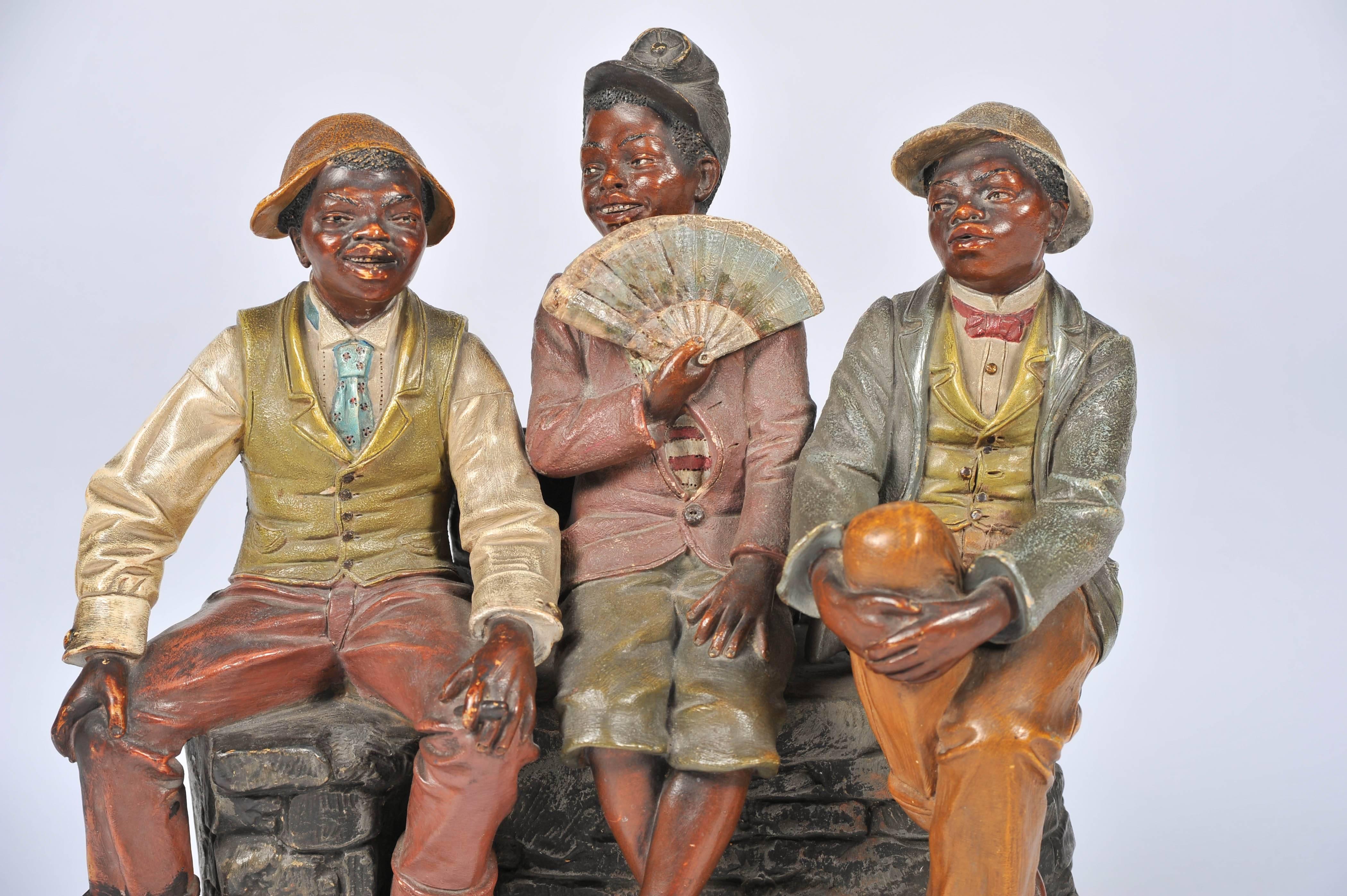 A very amusing late 19th century terracotta group, in the manner of 'Goldscheider' of three young black boys sitting on a wall.