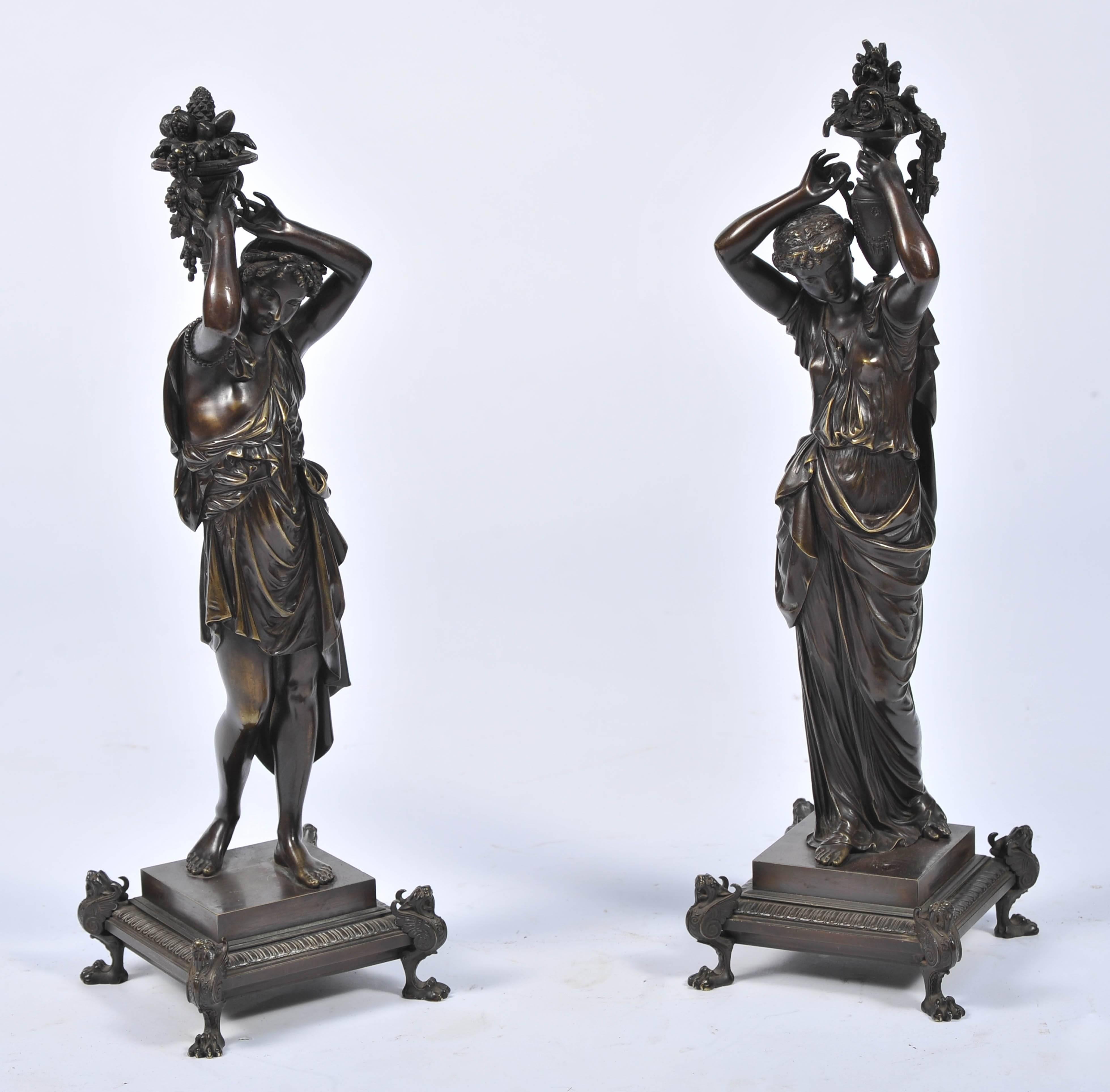 A good quality pair of 19th century French bronze statues depicting a male and female dressed in robes, carrying vases of flowers and fruit, mounted on square bases with claw feet.
