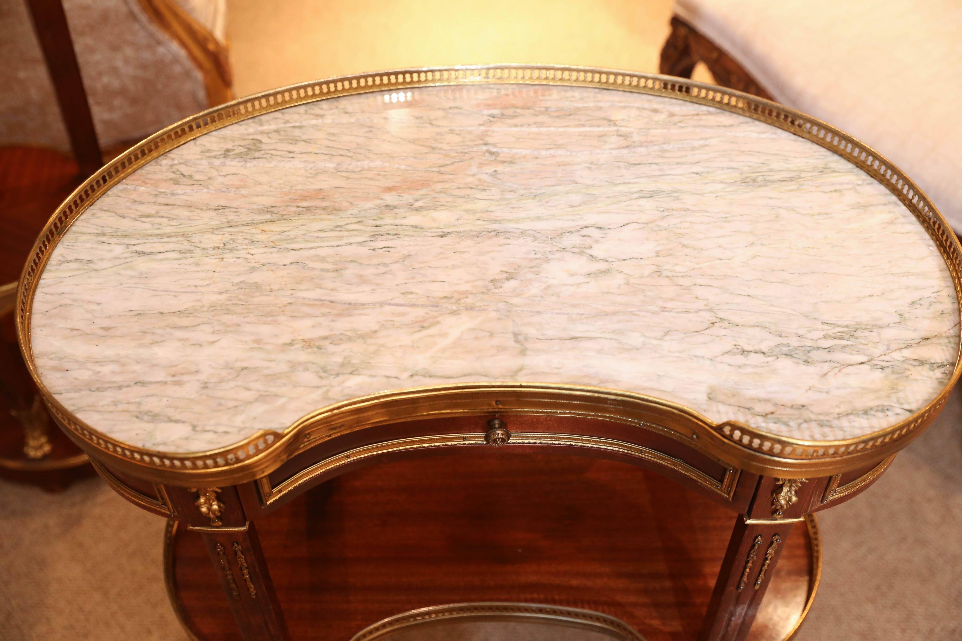 Early 20th century, the kidney form marble top within a three quarter pierced brass gallery, above a conforming frieze fitted with a single drawer, joined.
By fluted supports to a galleried lower shelf, raised on cabriole legs ending.
In sabots.