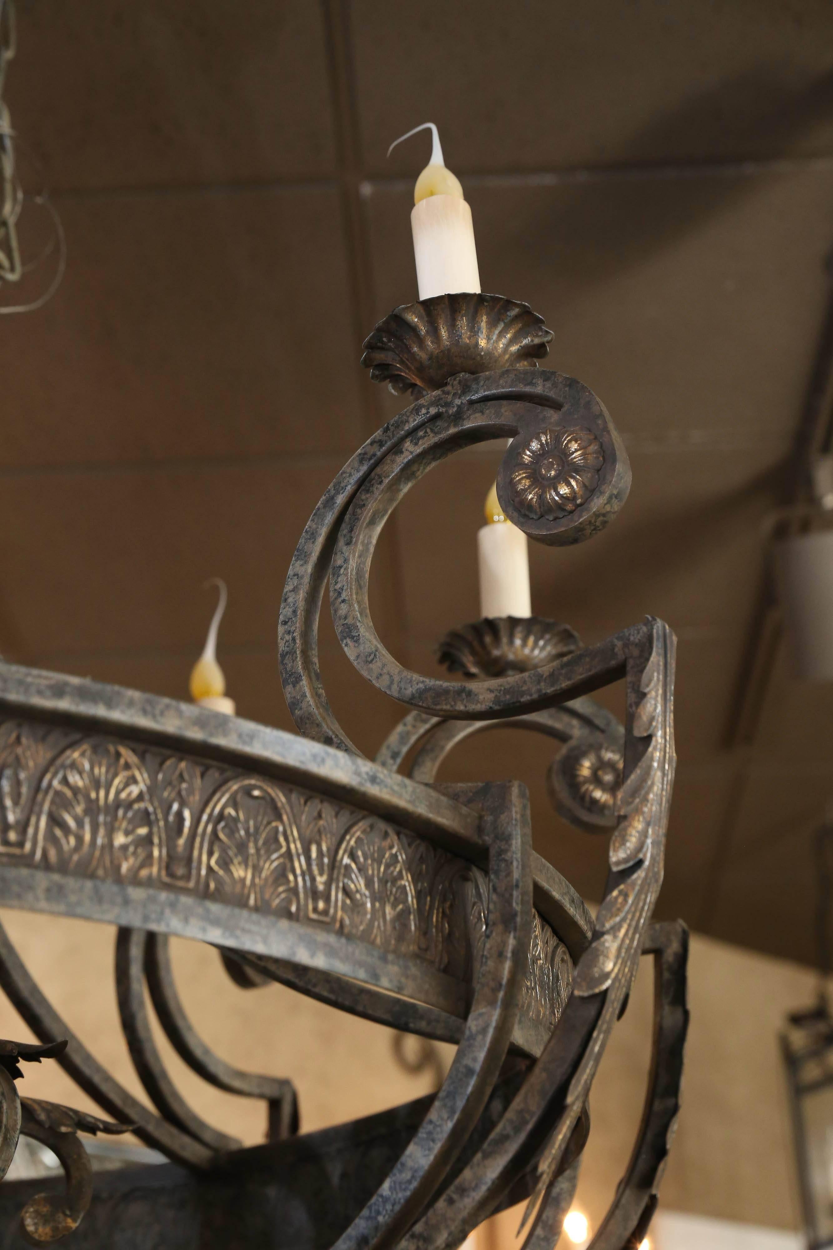 Large custom  iron designer chandeliers, Lightly painted highlights in gold.
The center urn form standard supports a central ring of acanthus leaves.
Issuing arms terminating in lights, flower head and foliate accents.
Throughout.