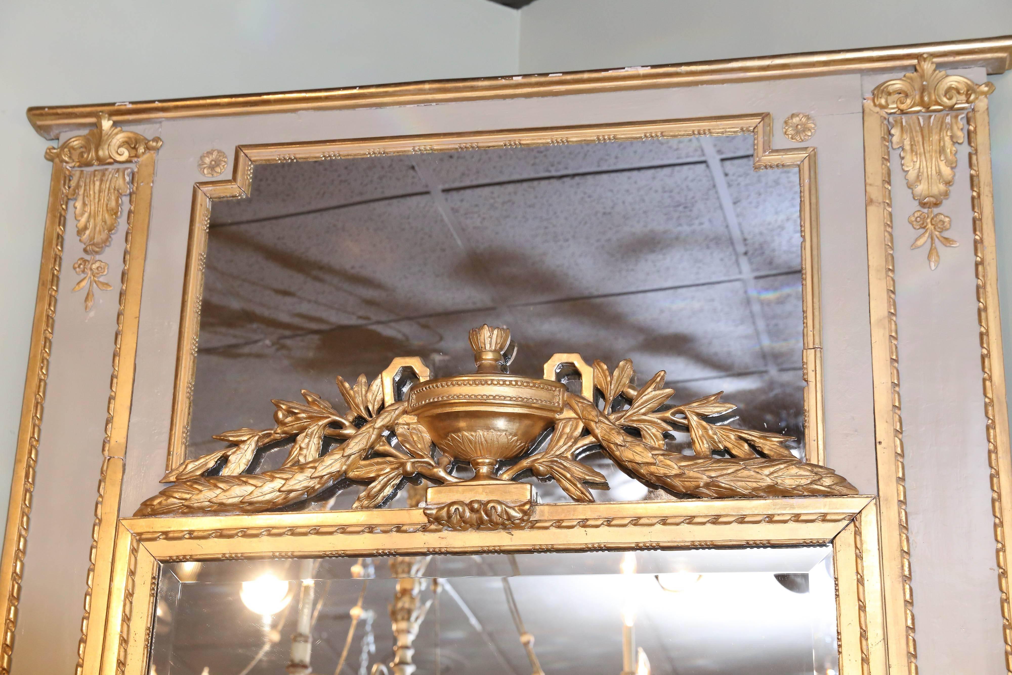 Le grand cadre ancien est peint dans une couleur grise française et les motifs
Ils sont à bord cordé et présentent un motif floral et de baies feuillagées sur les côtés.
Au centre, une urne embellit cette pièce avec un motif de feuille