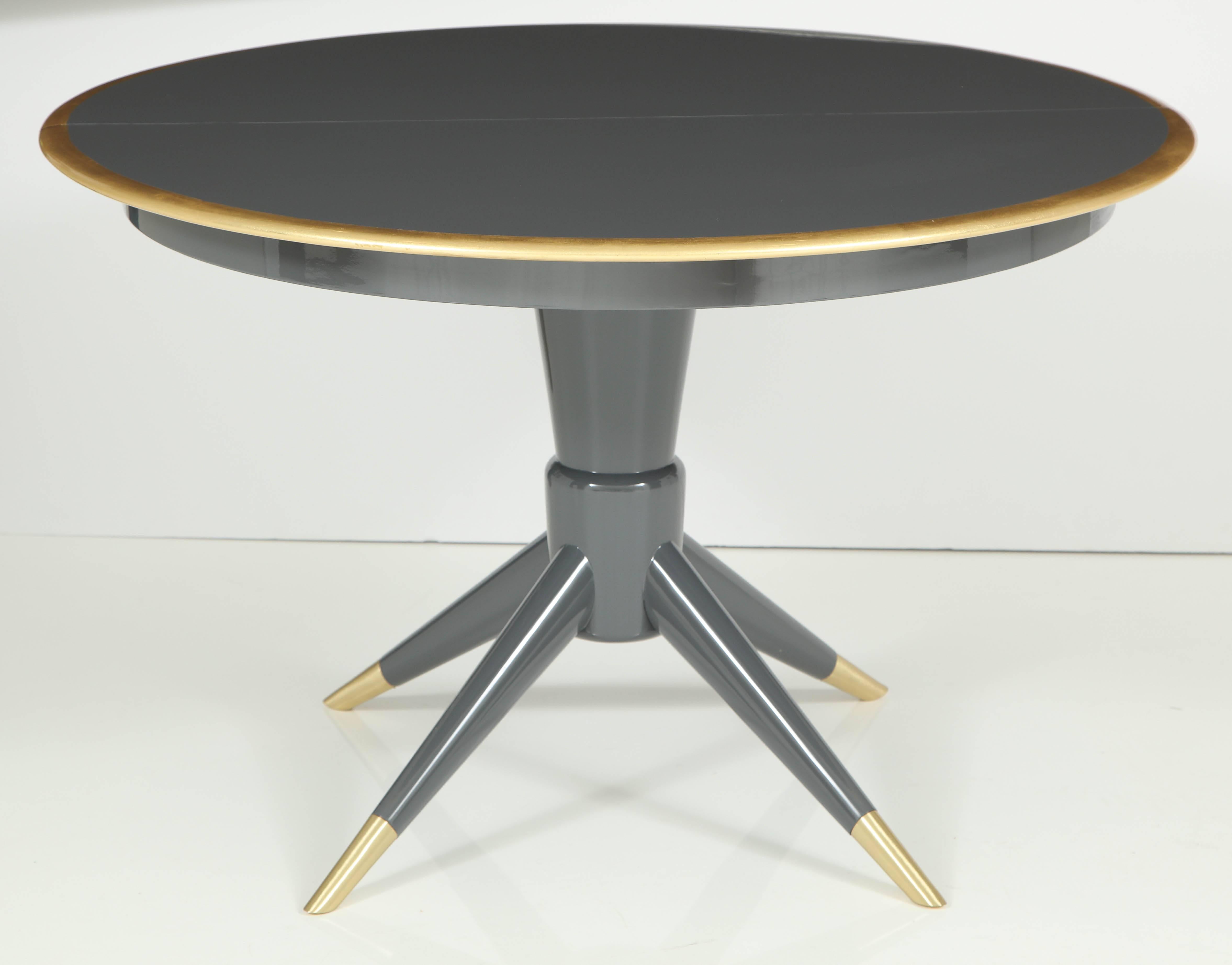 Swedish Modern dining table in a custom medium grey high gloss lacquer (grand piano finish) with a 22-Karat gold leaf band around perimeter. Each leaf is 14 inches wide. Pedestal table has four flared tapering legs finished in satin brass sabots.