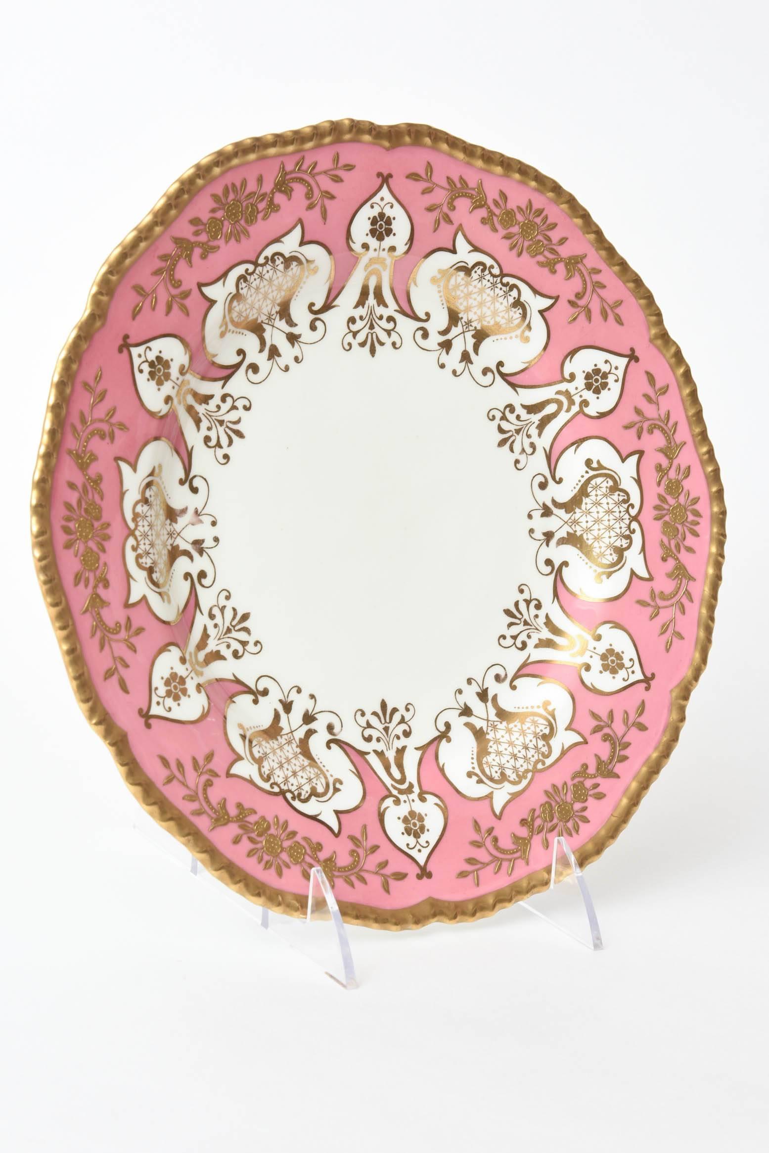 A stunning and vibrant set of pretty pink and gilt encrusted plates. 12 total. A beautiful scalloped and gadrooned edge and with custom retailer hall marks. An exotic cut-out design in the pink shoulder. A rare and special set in wonderful antique