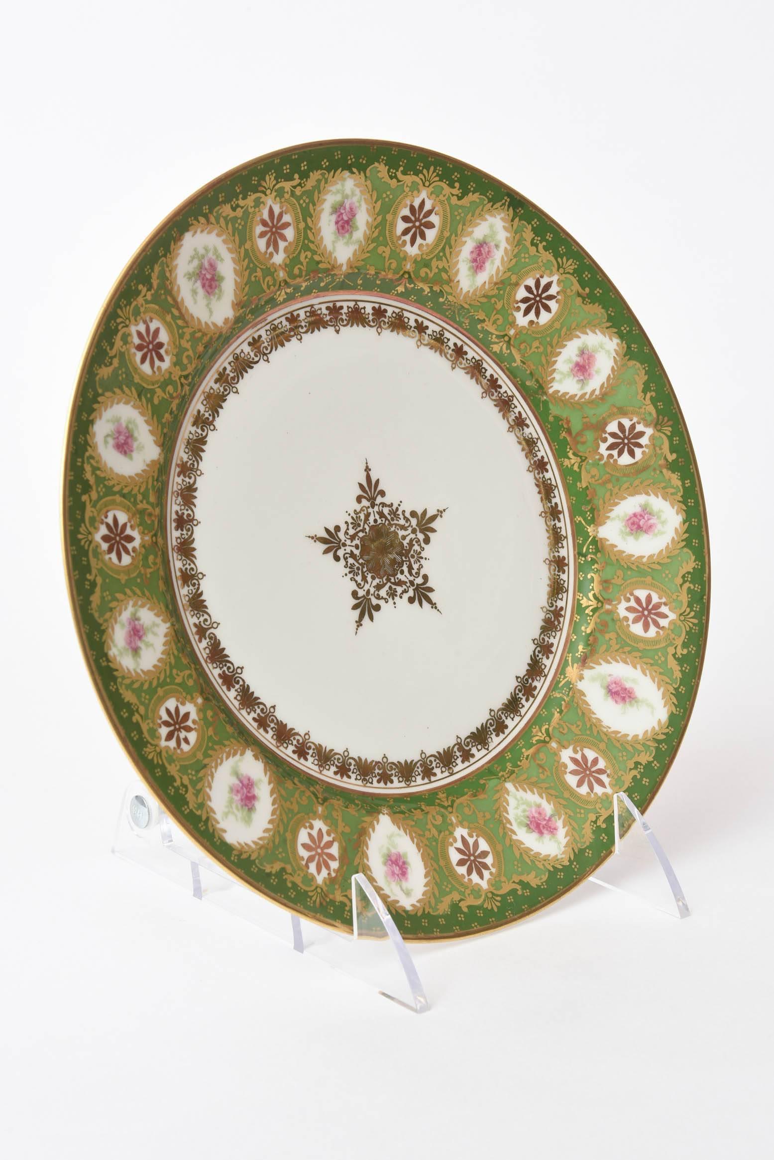 A lovely set of gilt trimmed dessert plates by Limoges with cartouches of elaborate hand painting and gilt decoration on a multi green shoulder. These also feature and a stunning five scroll star gilt medallion.