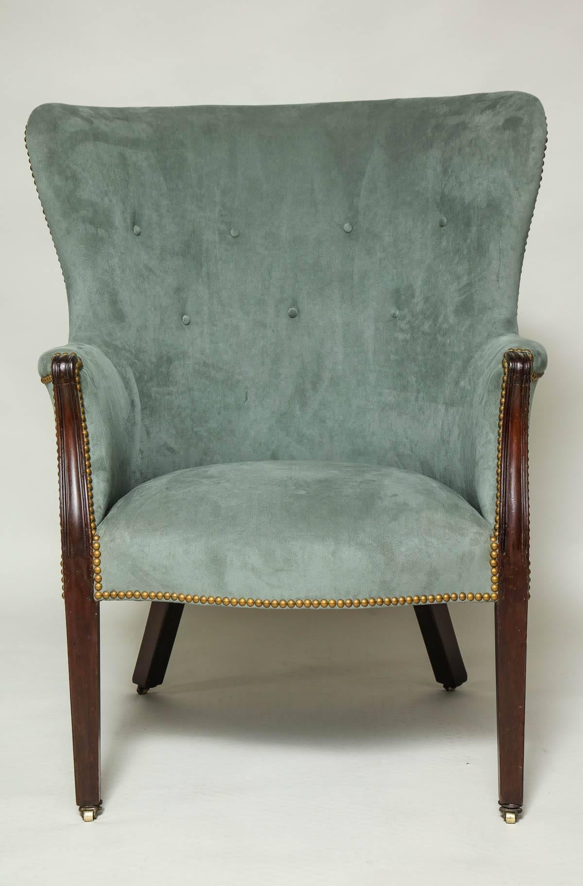 Fine 18th century George III mahogany wing chair with a barrel back. Arms with scroll carving, standing on square tapered and molded legs ending in original narrow brass casters. Newly upholstered in ultrasuede with close nailhead decoration,