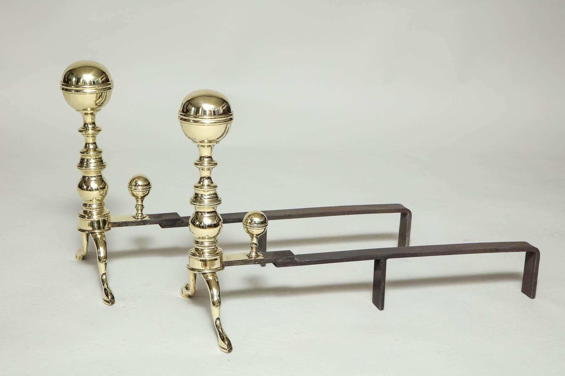 Pair of American Federal period brass andirons having canon ball finials with collar bands over ringed shafts and standing on spurred slipper feet, recently polished.