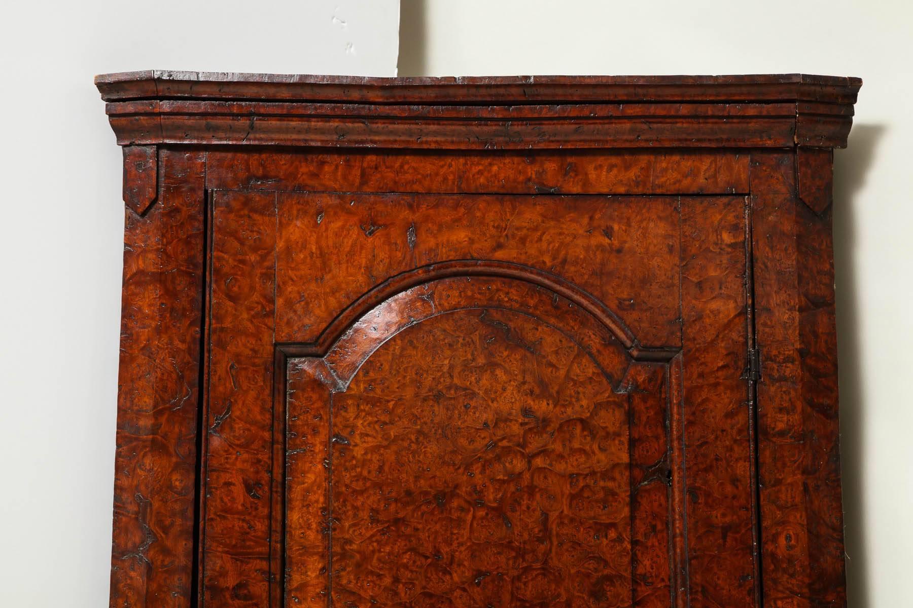 Very fine George II period hanging corner cover constructed of exceptionally grained solid burl elm, having a single door with solid arched raised panel. Interior with cupid bow scalloped shelves. The whole with exceptional graining and