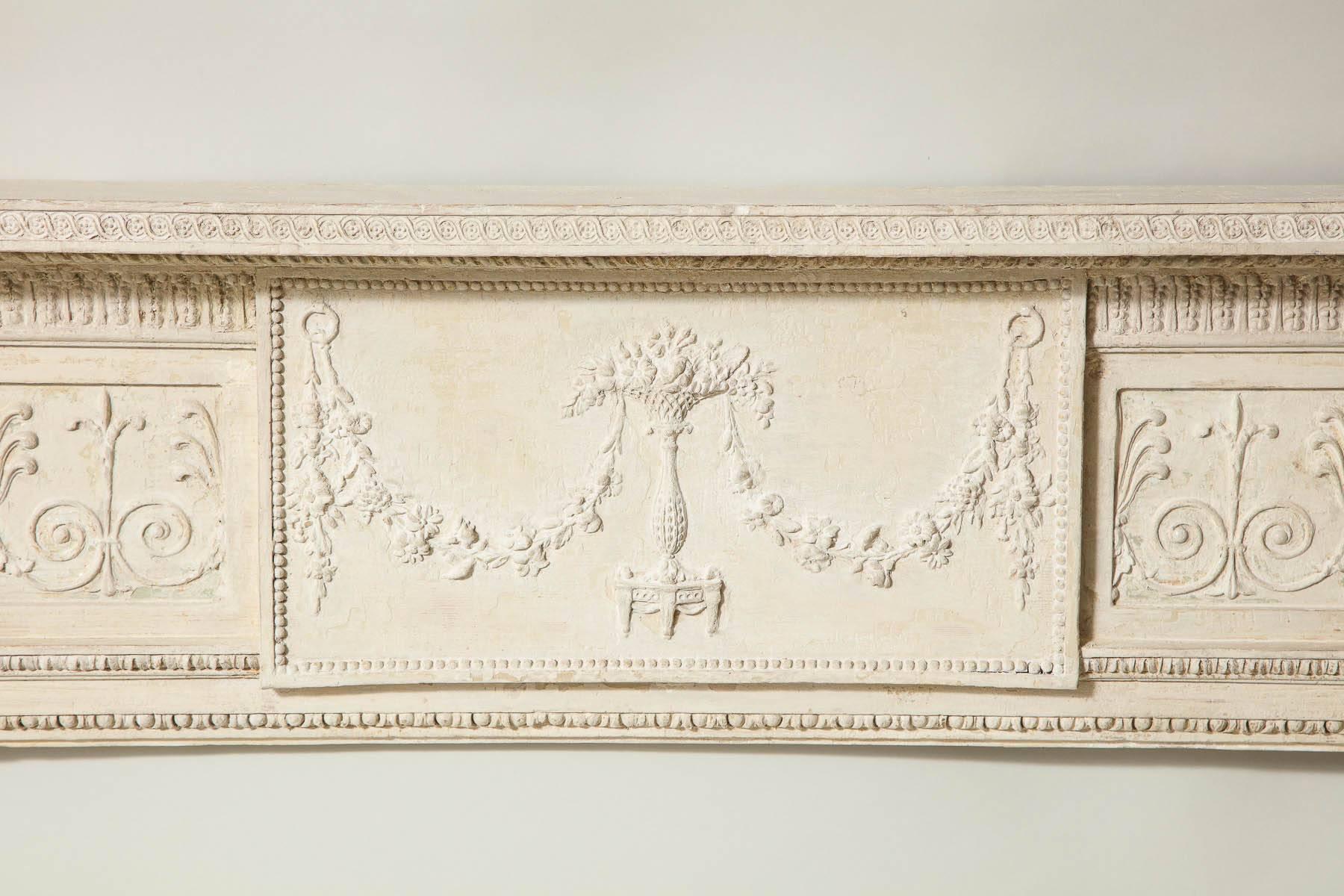 Very fine George III period mantel in original stone colored paint, the top shelf with guilloche carving over long acanthus carved molding, the center tablet with festooned swags draping from a tripod based jardinière, the two end panels with carved