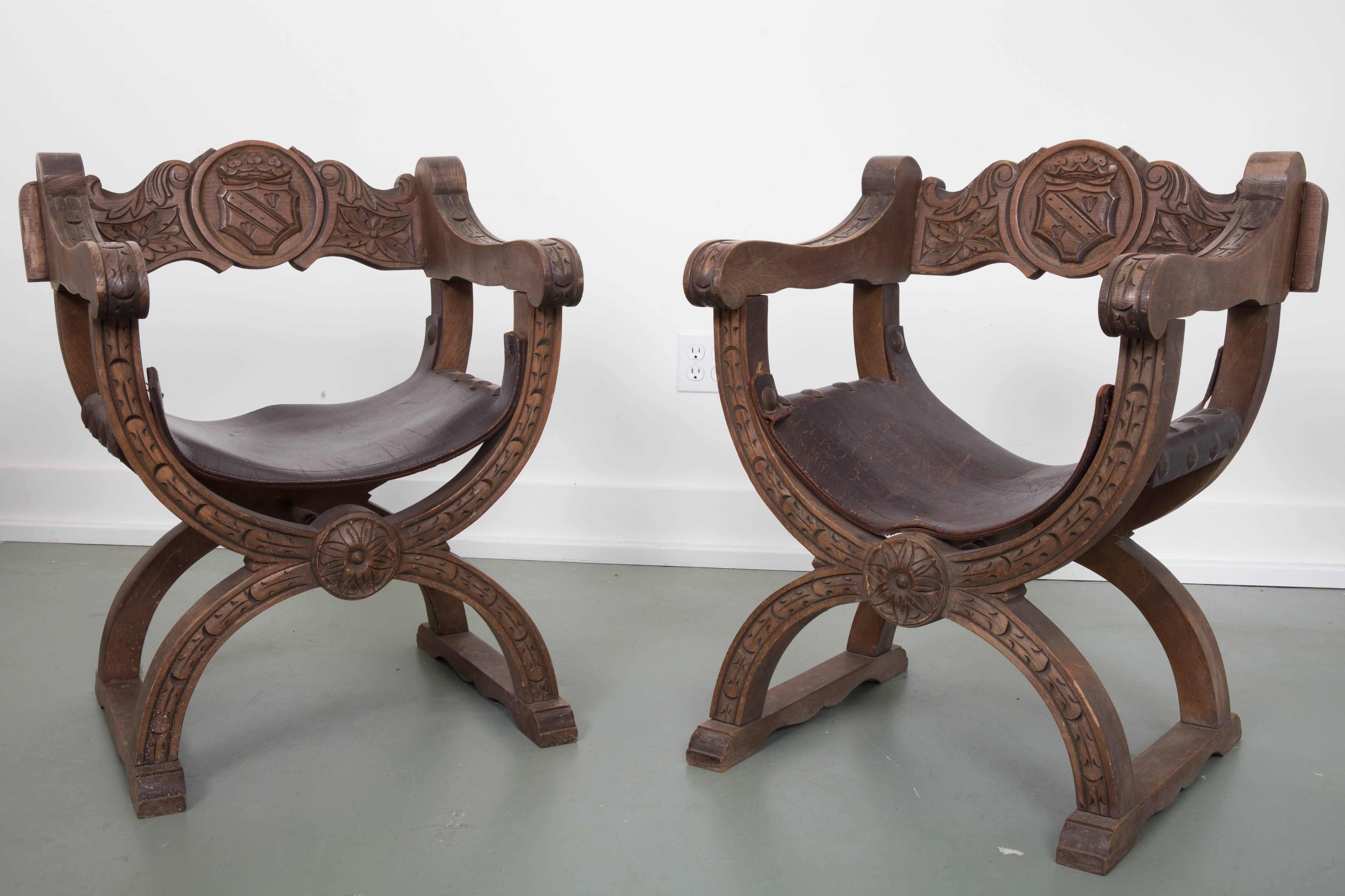 Pair of X-form Spanish Navarro Argundo chairs. Curale form seat surmounted with horizontal backsplat with carved shield and rosette raised on demilune supports joined by stretchers.