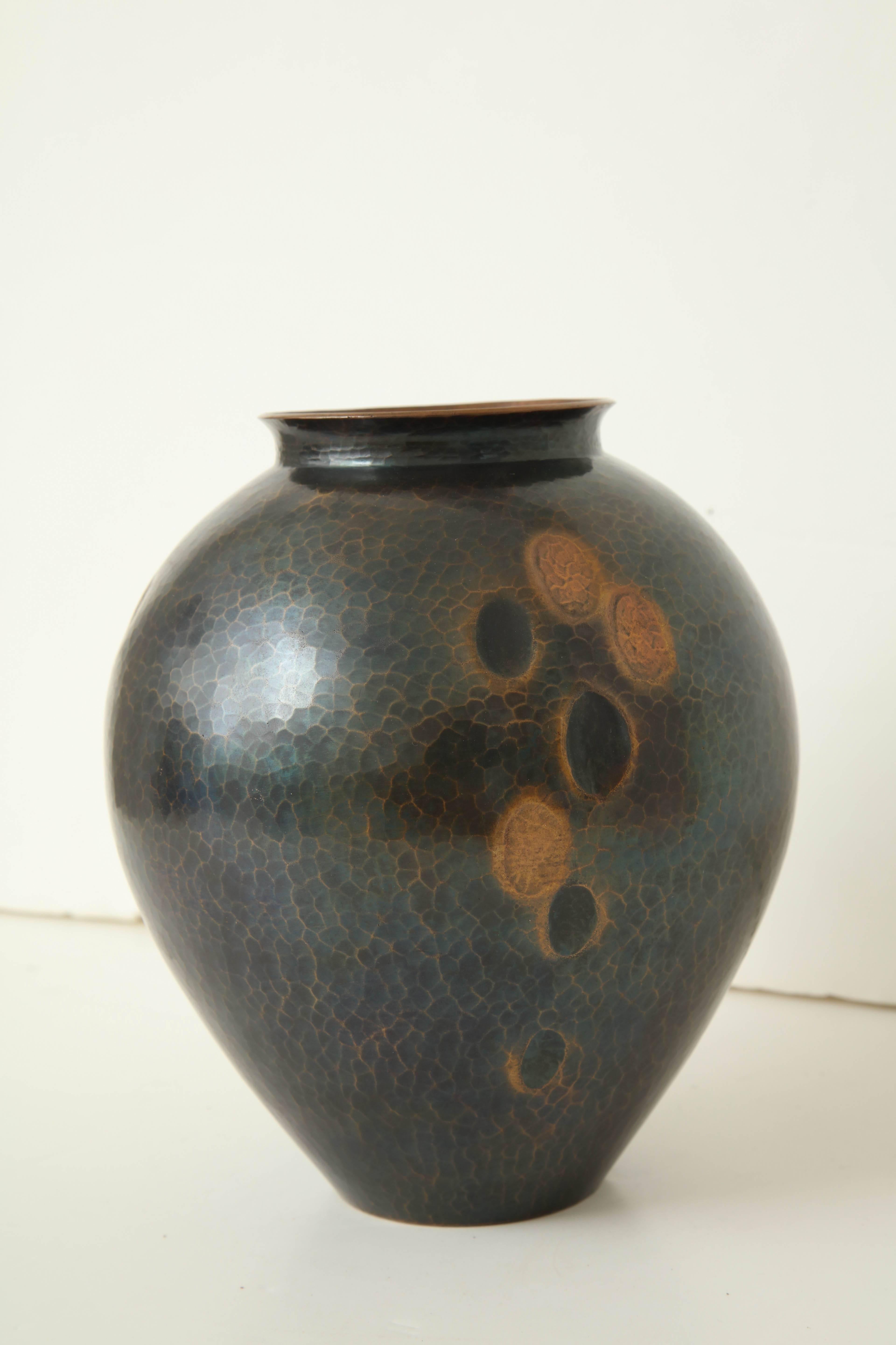 A Japanese Art Deco hammered copper vase with stylized oval repoussé decoration.
  