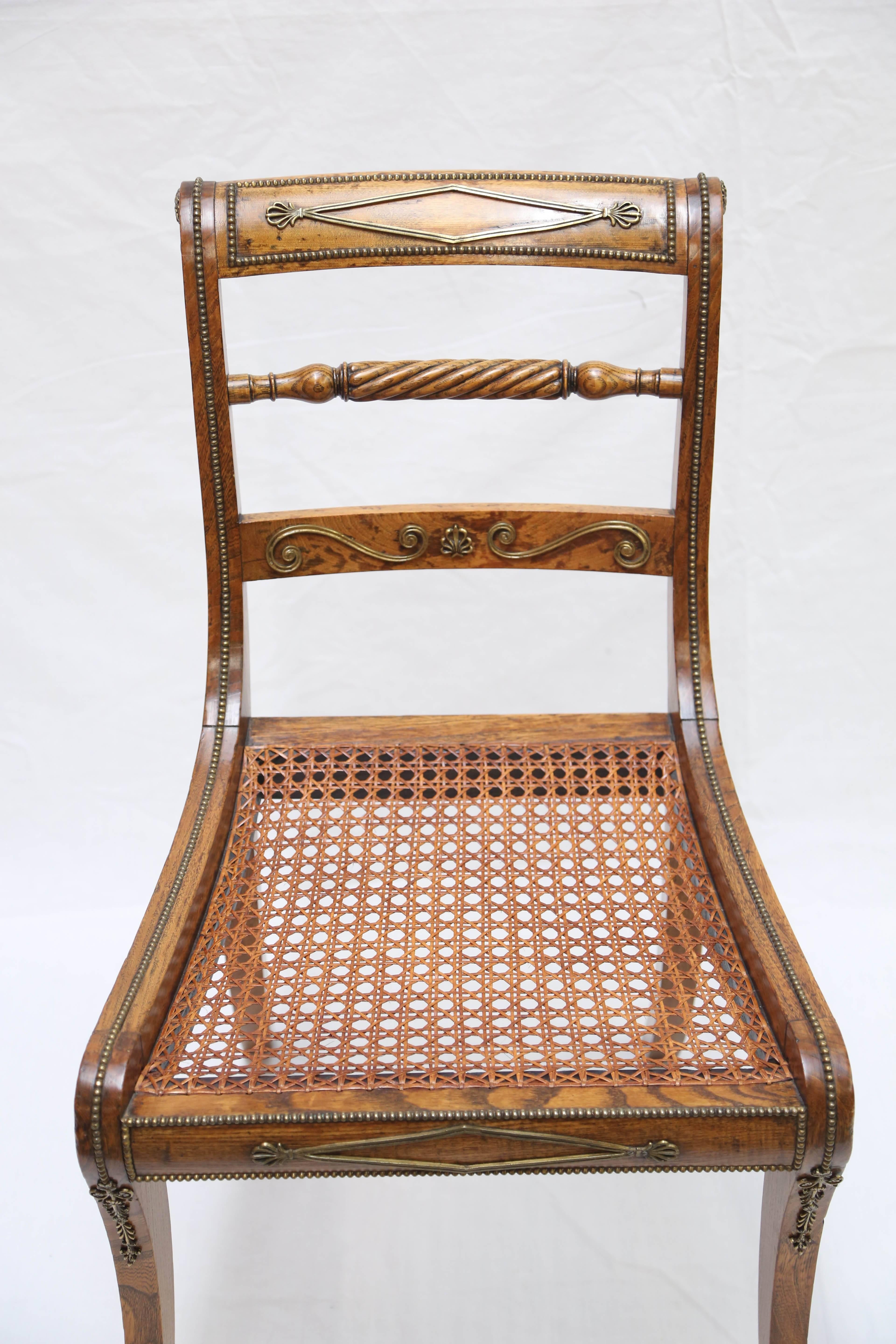 Comprising six side and two armchairs; each chair applied with beaded brass banding overall; the top rail centered mounted with a brass diamond with honeysuckles to the corners, over a spiral fluted back splat; the caned seat with seat cushion