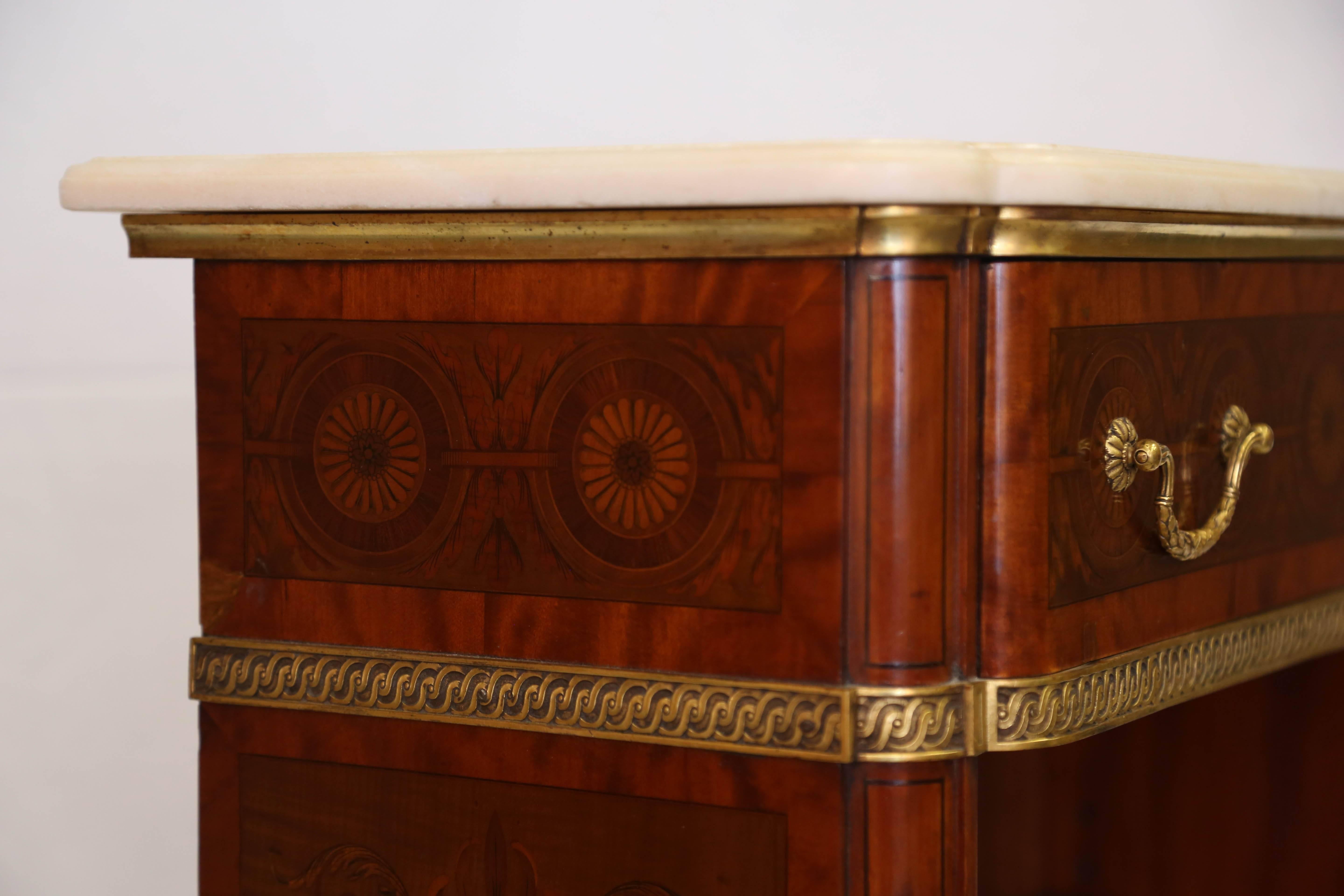 The rectangular white marble top with eared corners over an gilt-metal bound edge and frieze inlaid with guilloche marquetry beautifully designed to incorporate the hardware, over two adjustable shelves, on tapering feet with decorative sabots.