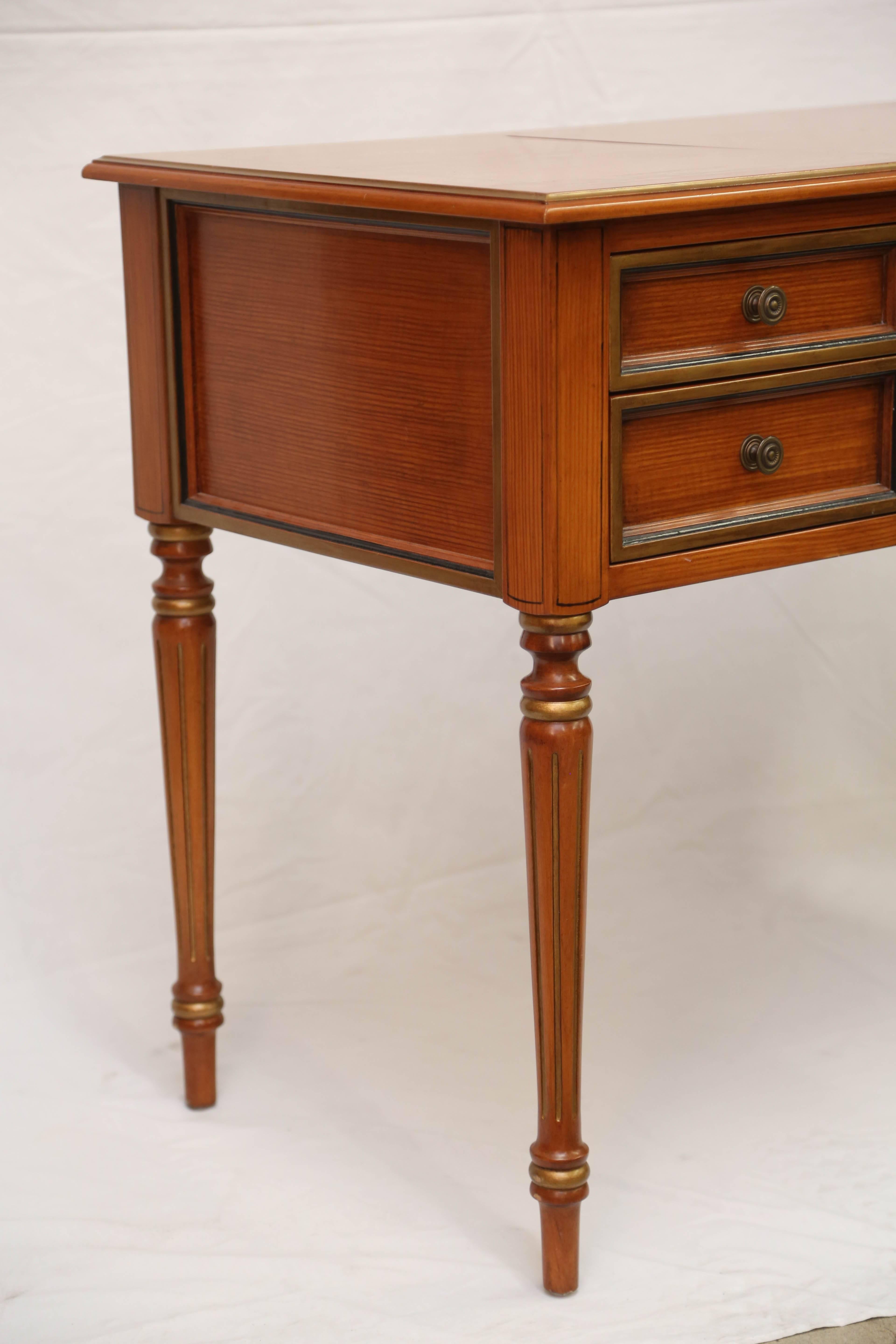 The rectangular top with hinged center panel lifting to a vanity mirror and storage compartment, over a frieze with drawers with gilt and bonded detailing flanking the kneehole; raised on turned tapering legs. Kneehole measures 25.5