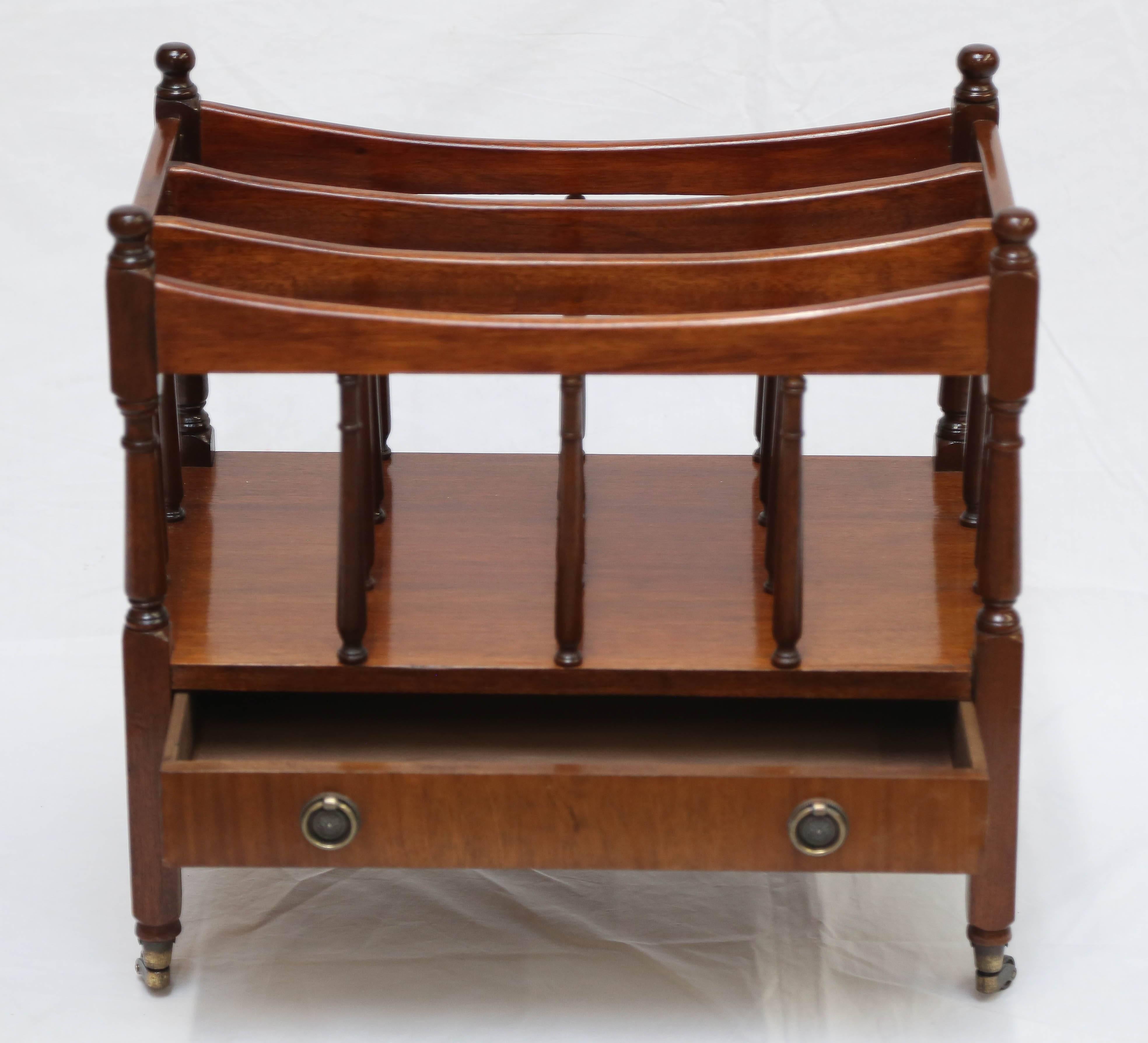 Featuring four compartments over a drawers; on brass casters. The canterbury was the original magazine/newspaper rack. This period example is elegant in its simplicity.