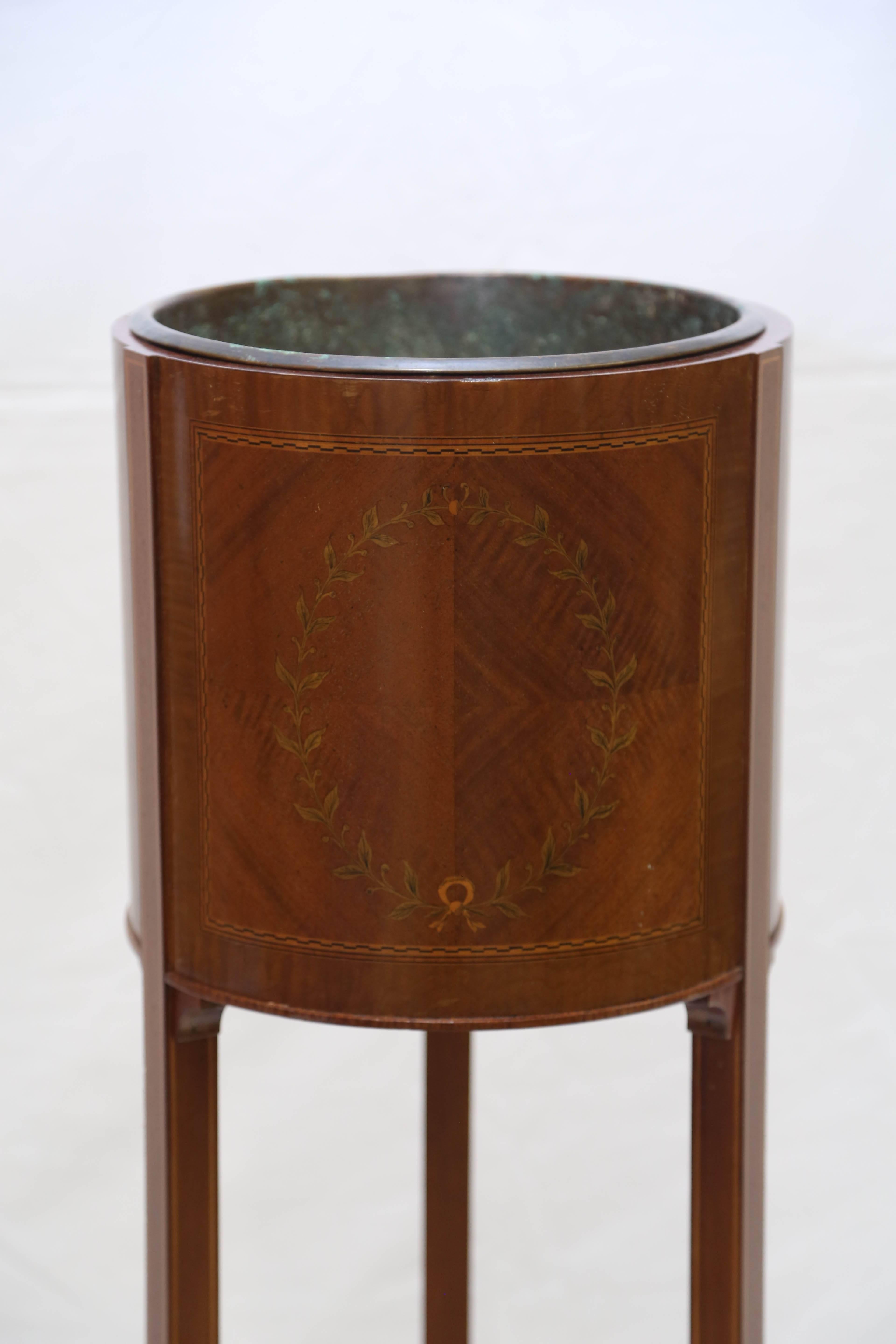 The mahogany stand inlaid with a ribbon-tied laurel wreath with checkerboard banding on a quarter-veneered ground; on tapering splayed legs joined by a stretcher; incorporating a 10