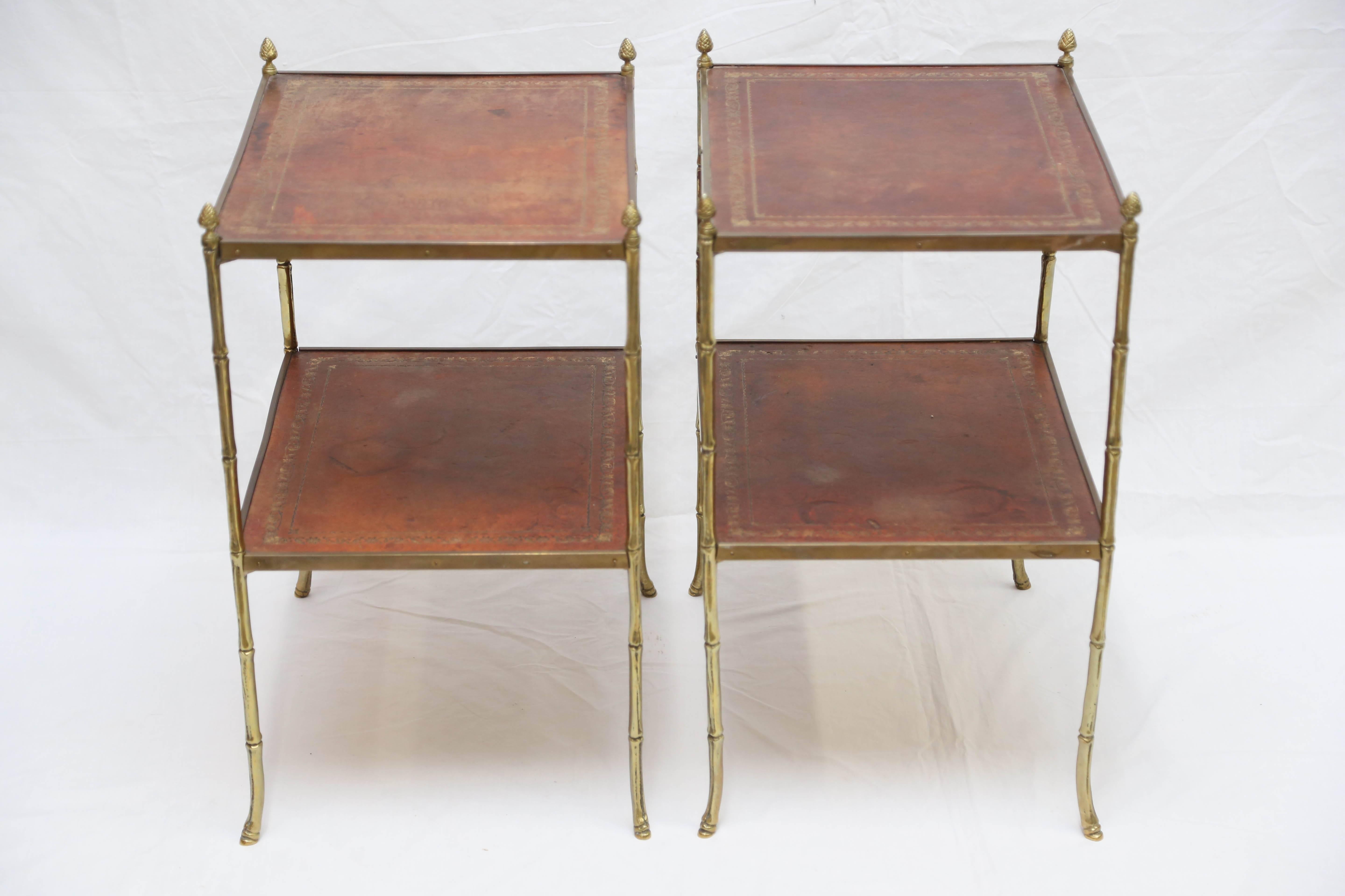 Each table with two gilt-tooled leather-lined shelves set within a brass frame with faux bamboo uprights surmounted by pine cone finials.