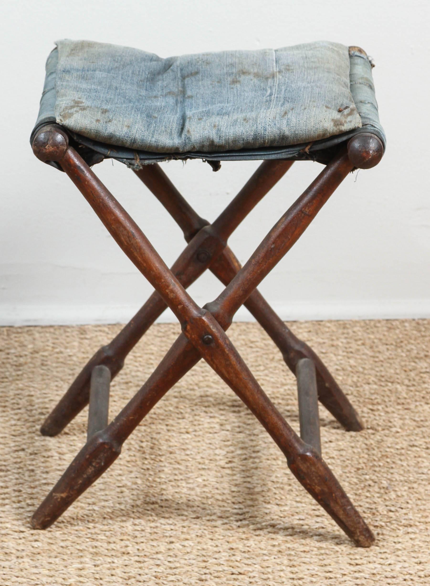 Early 20th century folding stool. Flat pillow and crosspiece made from faded but still sturdy indigo denim jeans.