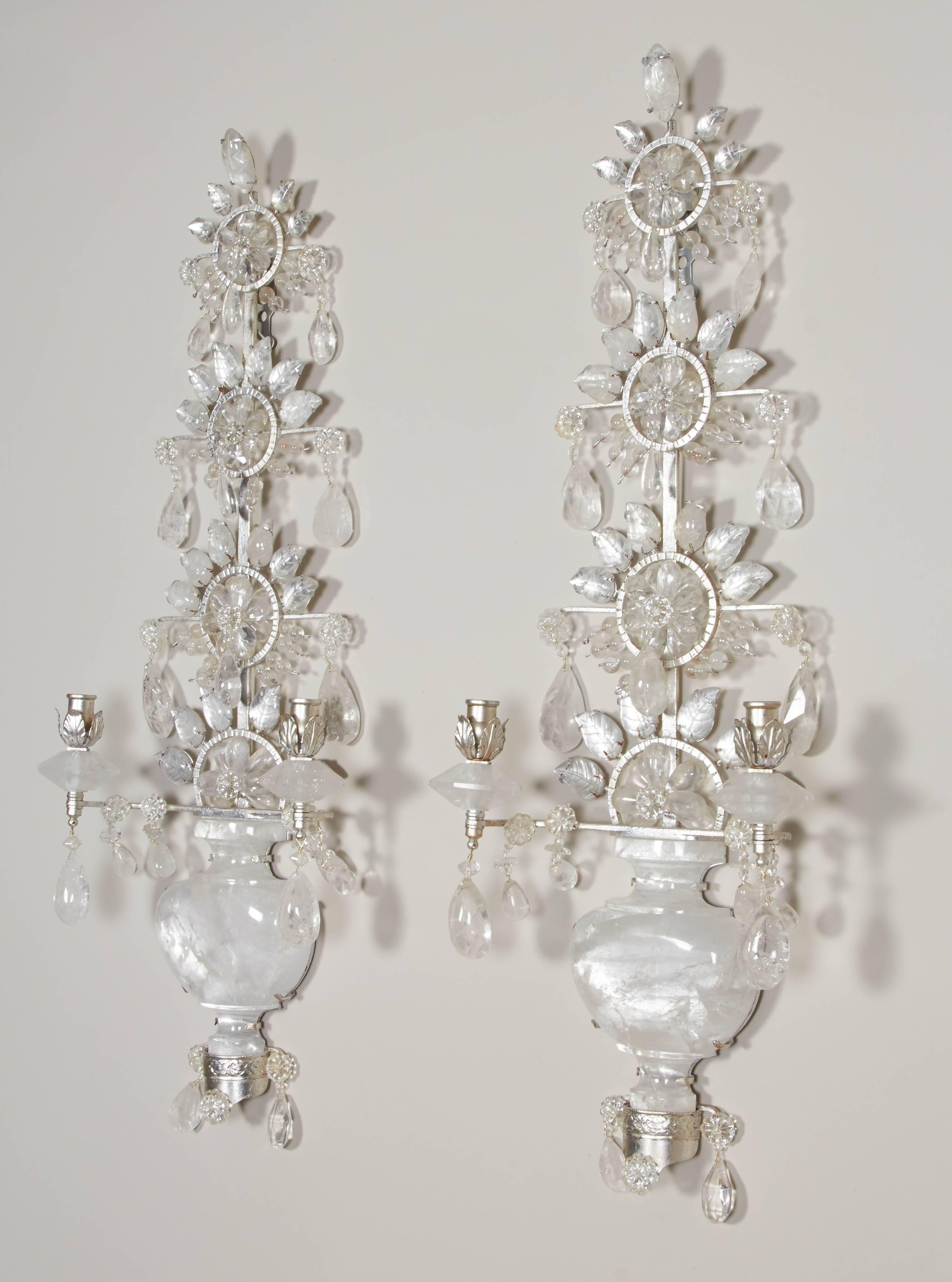 A pair of silvered metal two-light sconces with backplate in the form of a Chinese vase in three sections of carved rock crystal. The upper section continuing into three rows of oversized rosettes formed by rock crystal beads encircled by carved