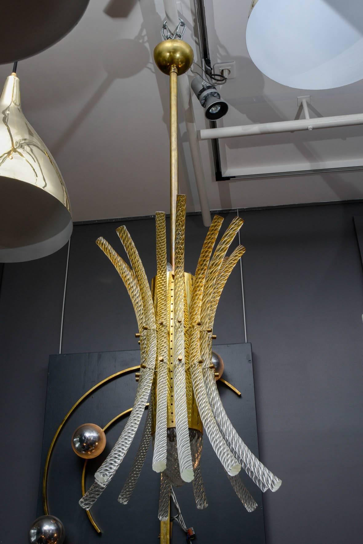 Pair of pendants made of a brass perforated centerpiece holding the lights, and 12 bent and swirled Murano glass rods, tinted at the top.
