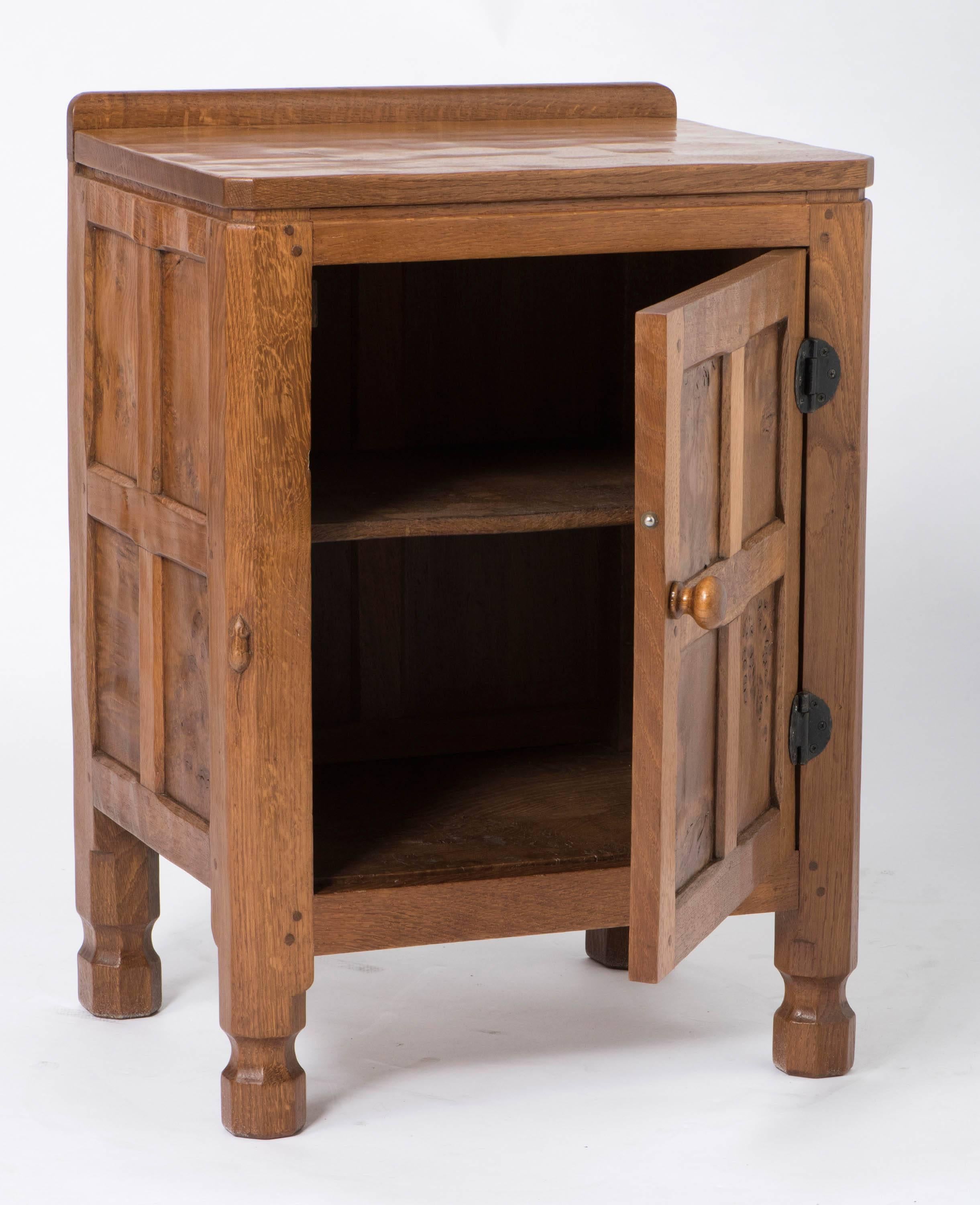 A rare and early oak bedside Cabinet by Robert “Mouseman” Thompson 
Adzed work to oak.
The panels to the sides and the door set with burr oak.
Wasted octagonal feet.
Metal work hinges.
Carved mouse signature, 
England, circa 1930
Measures: 66