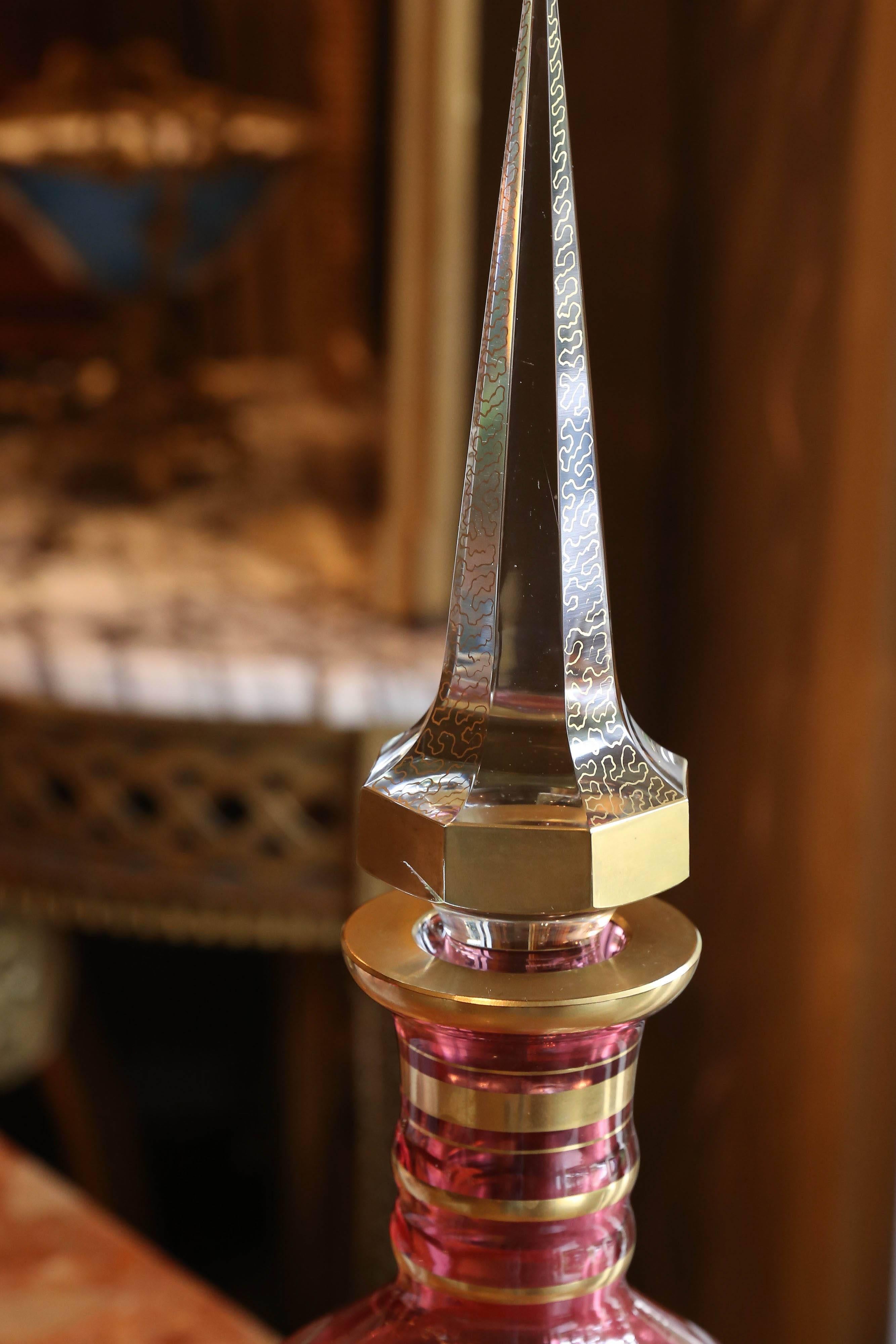 Czech cranberry cut to clear gilt glass decanter, having a large tapered
Stopper decorated with vermicelli, over a ribbed neck, circular cut
Pattern to shoulder of body, gilt scroll band at centre, rising on a circular
foot.