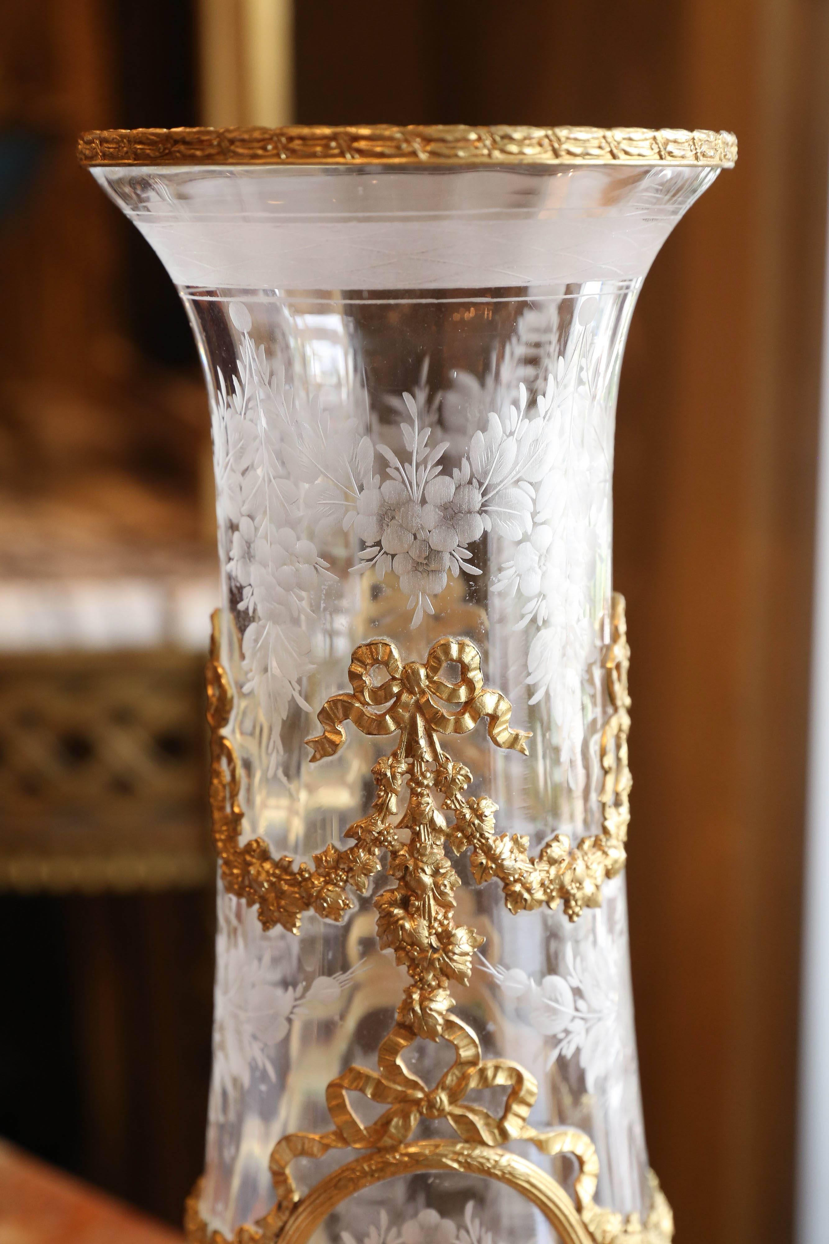 Beautiful glass vase engraved with floral swags and pendants, under gilt
Metal bowknots supporting swags of flowers and reserving further 
Engraved floral sprays, supported on a gilt metal foot marked France.