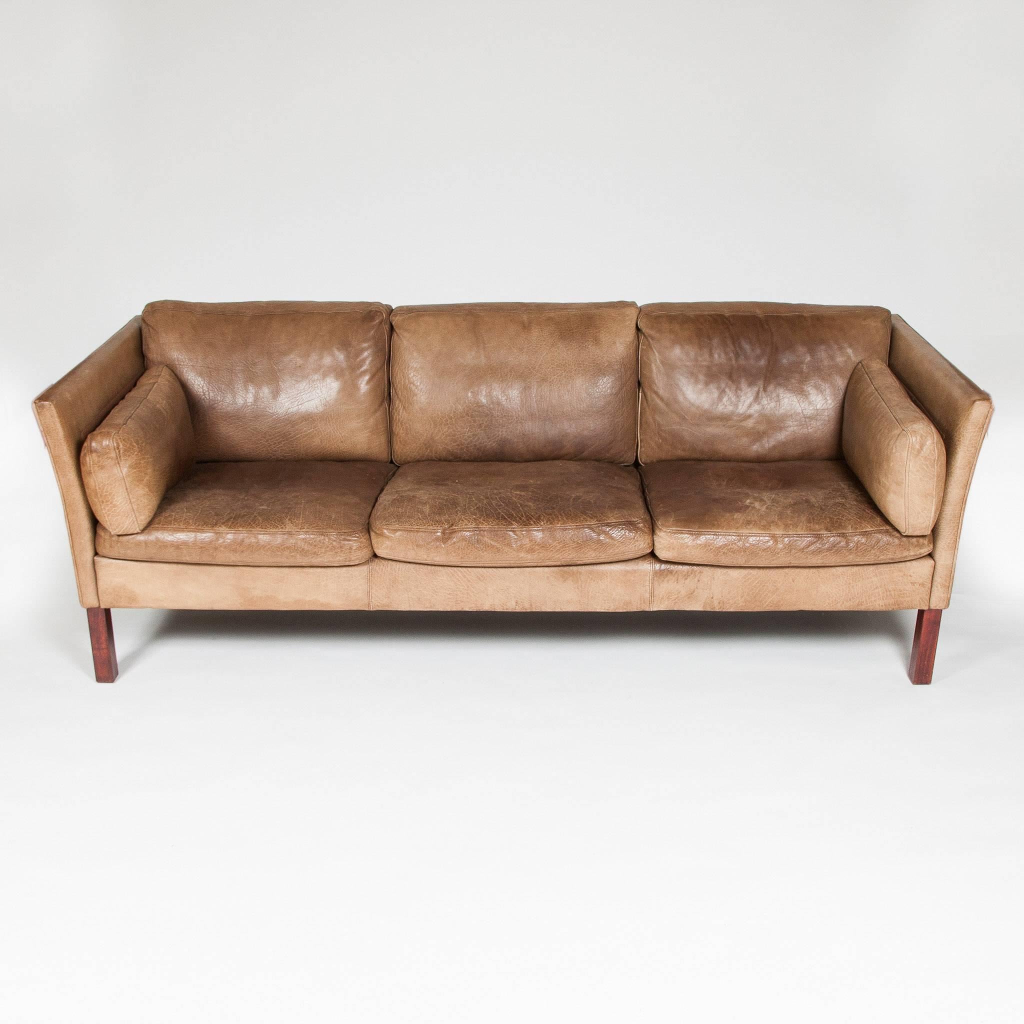 A mid-1970s three seat sofa upholstered in patinated light brown buffalo hide, with stained beech legs.

Designed by Mogens Hansen in 1971 for MH Møbler A/S of Hasselager, Denmark.