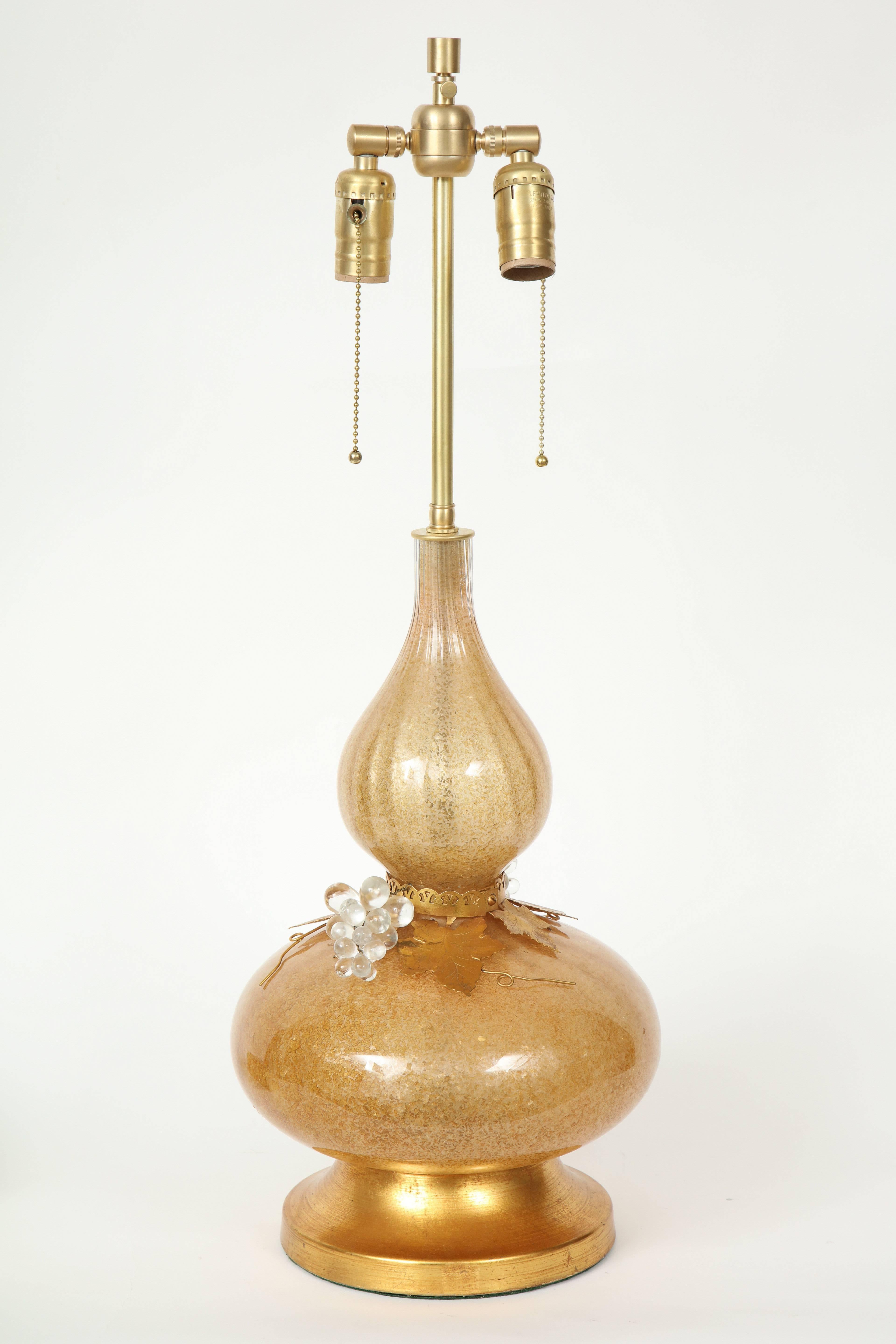 Mid-Century Murano glass genie bottle shaped lamps in a rich gold tone with crushed glass pieces applied to the interior. 22 karat gilt washed leaves and clear glass grapes adorn the cinched middle. Lamps rest on 22 karat gold washed brass bases.
