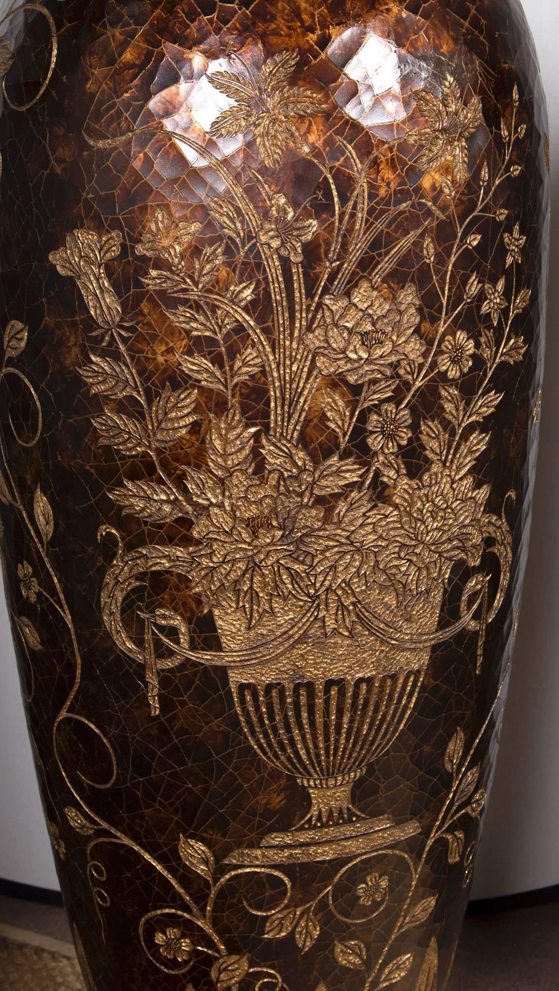 The pair have a large bulbous body with a tall, flairing neck opening. They appear to be made of copper, covered by a lacquer, crackled to resemble aged leather. They are incised with gold all around, with vines, flowers in urns and stylized leaves.