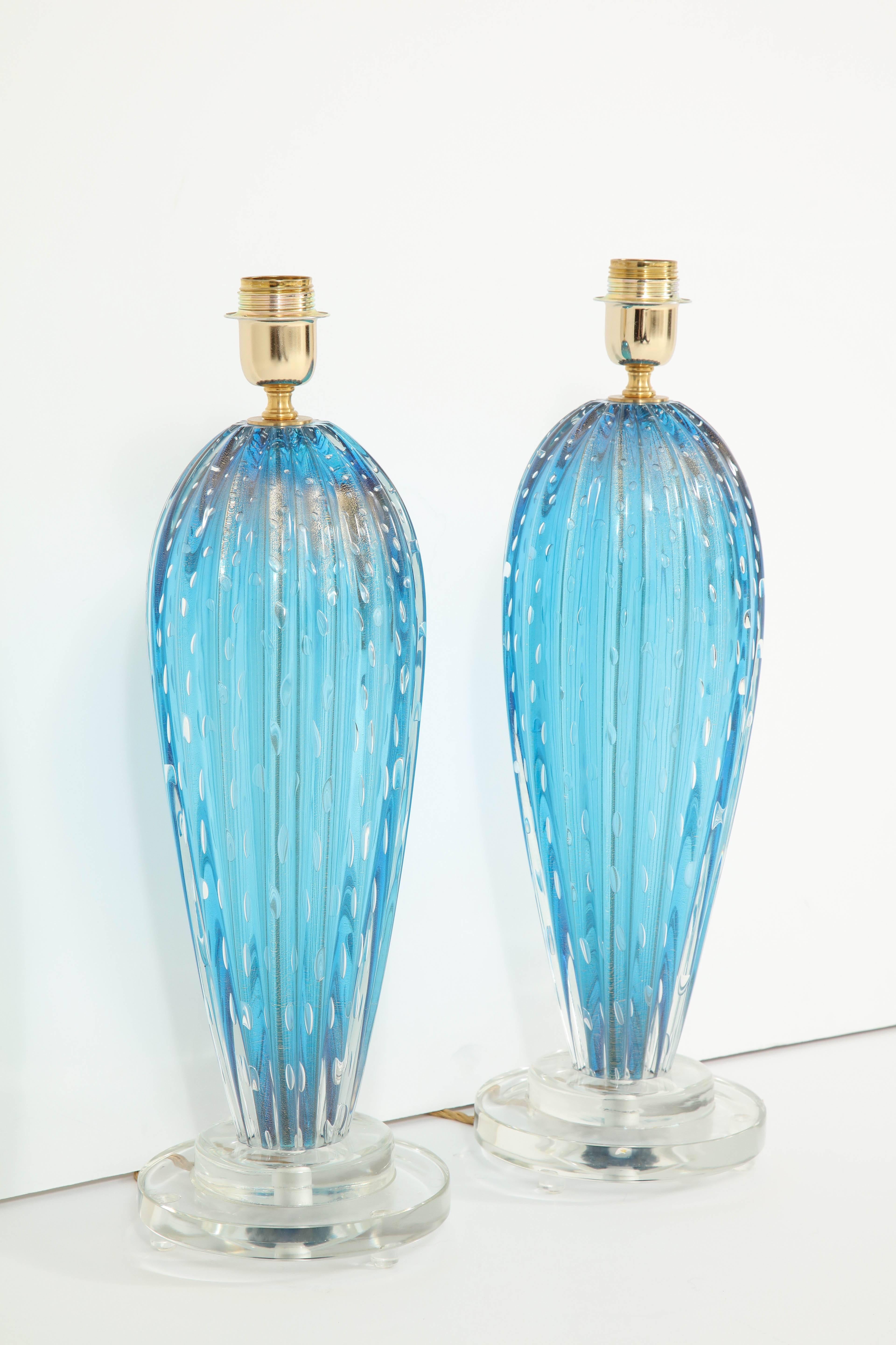 A pair of Murano blown glass lamps in a stunning shade of blue. The lamps were created using the Pulegoso technique, resulting in the appearance of small "bubbles." The base is solid, clear Murano glass.