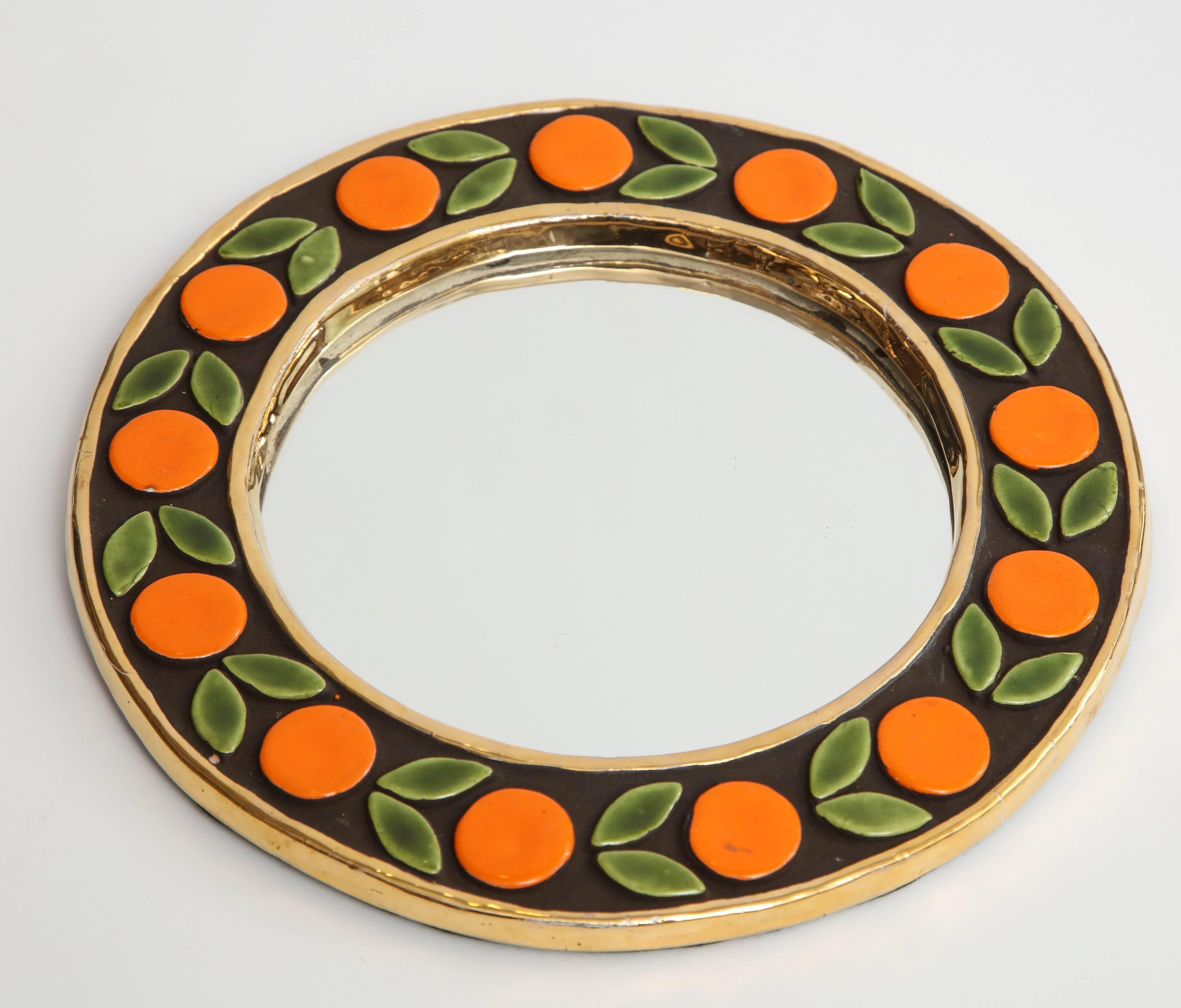 A lovely small, round mirror created by Mithé Espelt in France, circa 1960. The frame is decorated in a gold metallic glaze and the design in a shiny enamel of rich brown, orange and green.