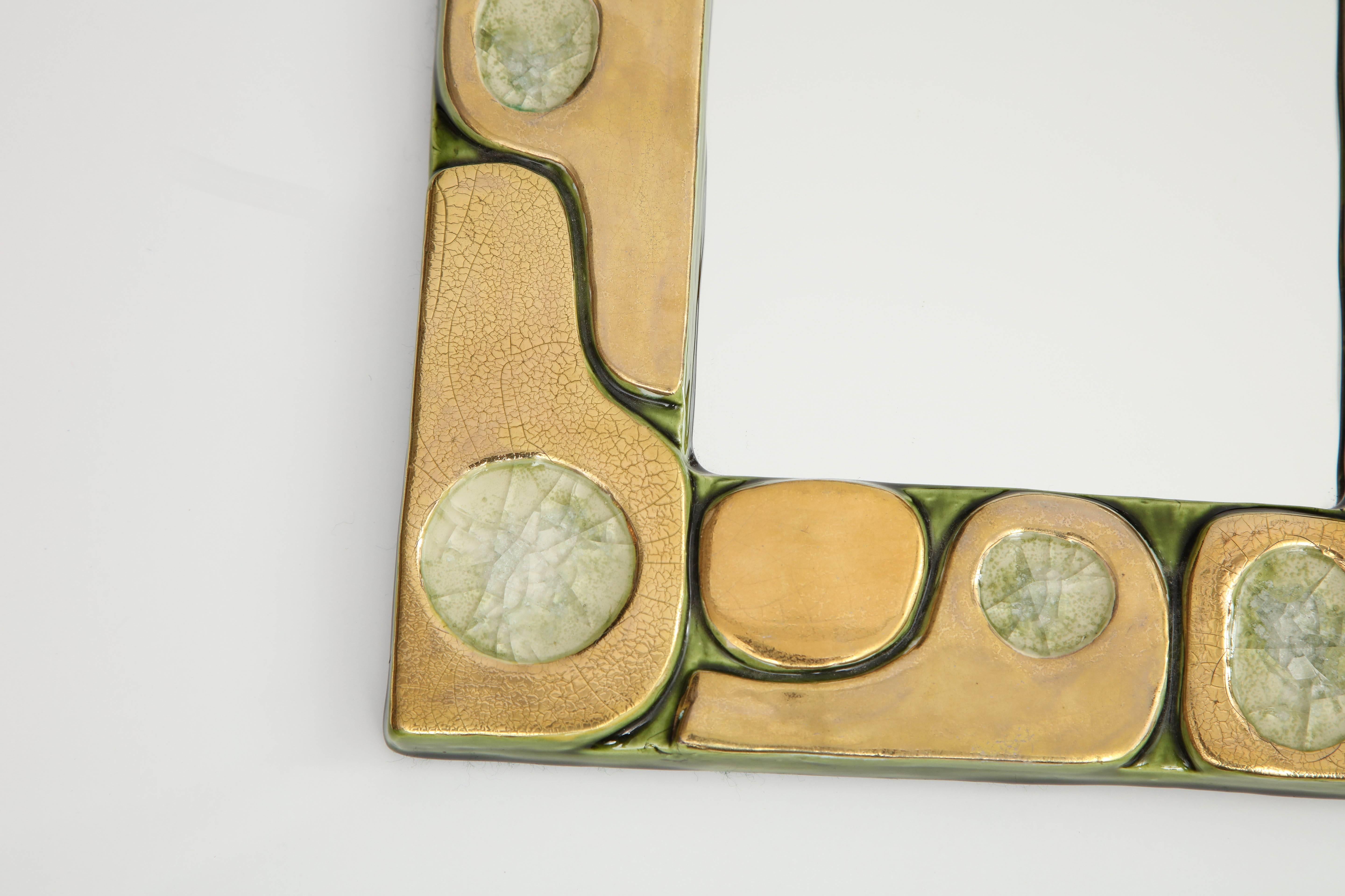 A small, but stunning mirror created by Mithé Espelt, circa 1960, in France. The mirror is composed of pieces of stone within a gold crackle glazed ceramic frame. The border of the frame is painted in a green enamel and the back is felt.