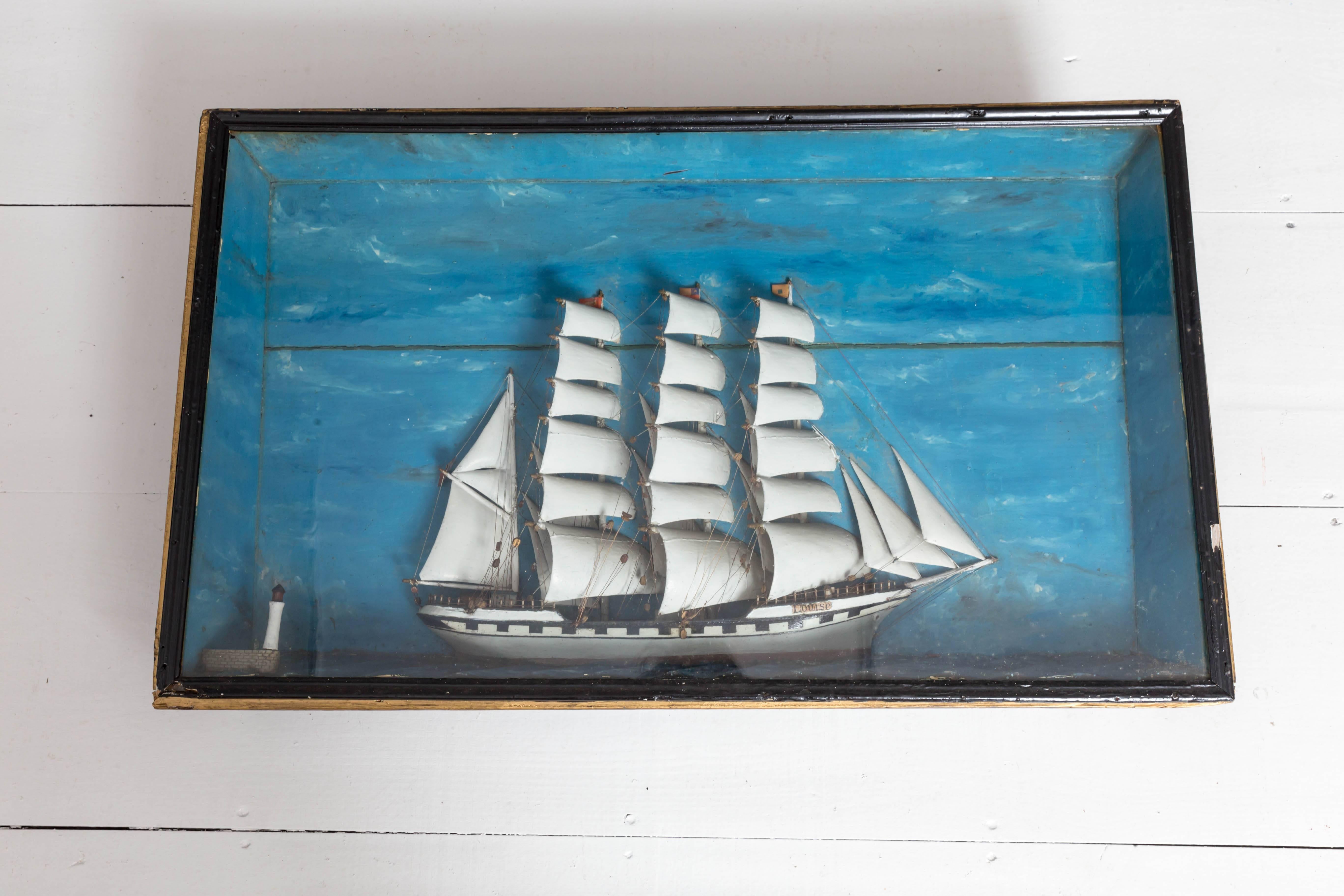 French ship diorama with a large Schooner and small lighthouse. Hand-carved out of wood which includes the hull, sails, masts, and accoutrements. Mounted in a deep mitered wood frame with painted sea and sky background.