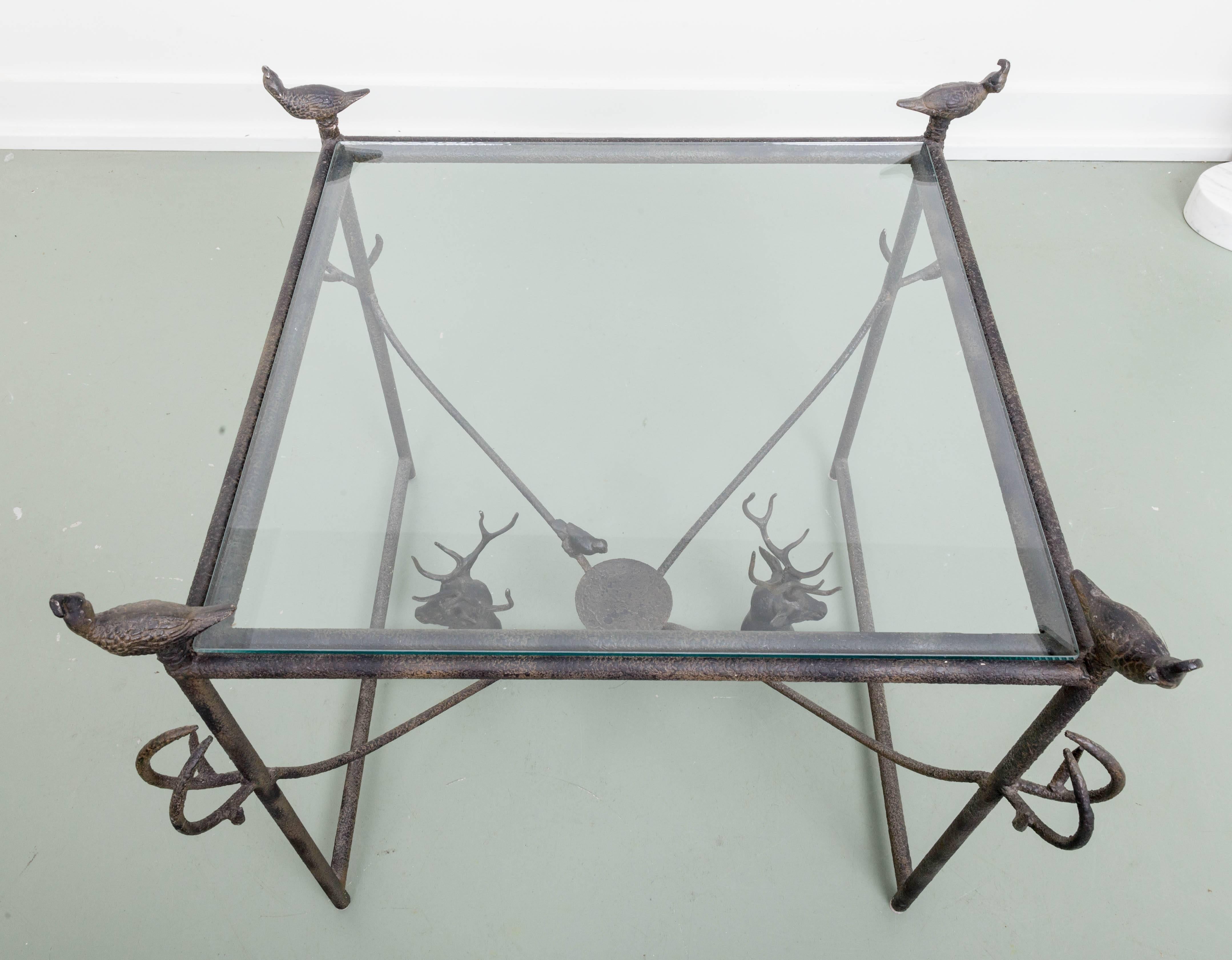 Perfect hunting lodge table, metal table with decorative rough applied finish. Four Quail finials. Glass top. H-stretcher with connecting branches to legs finishing up with stylized Antlers on legs. Two four points stag heads on stretcher flanking