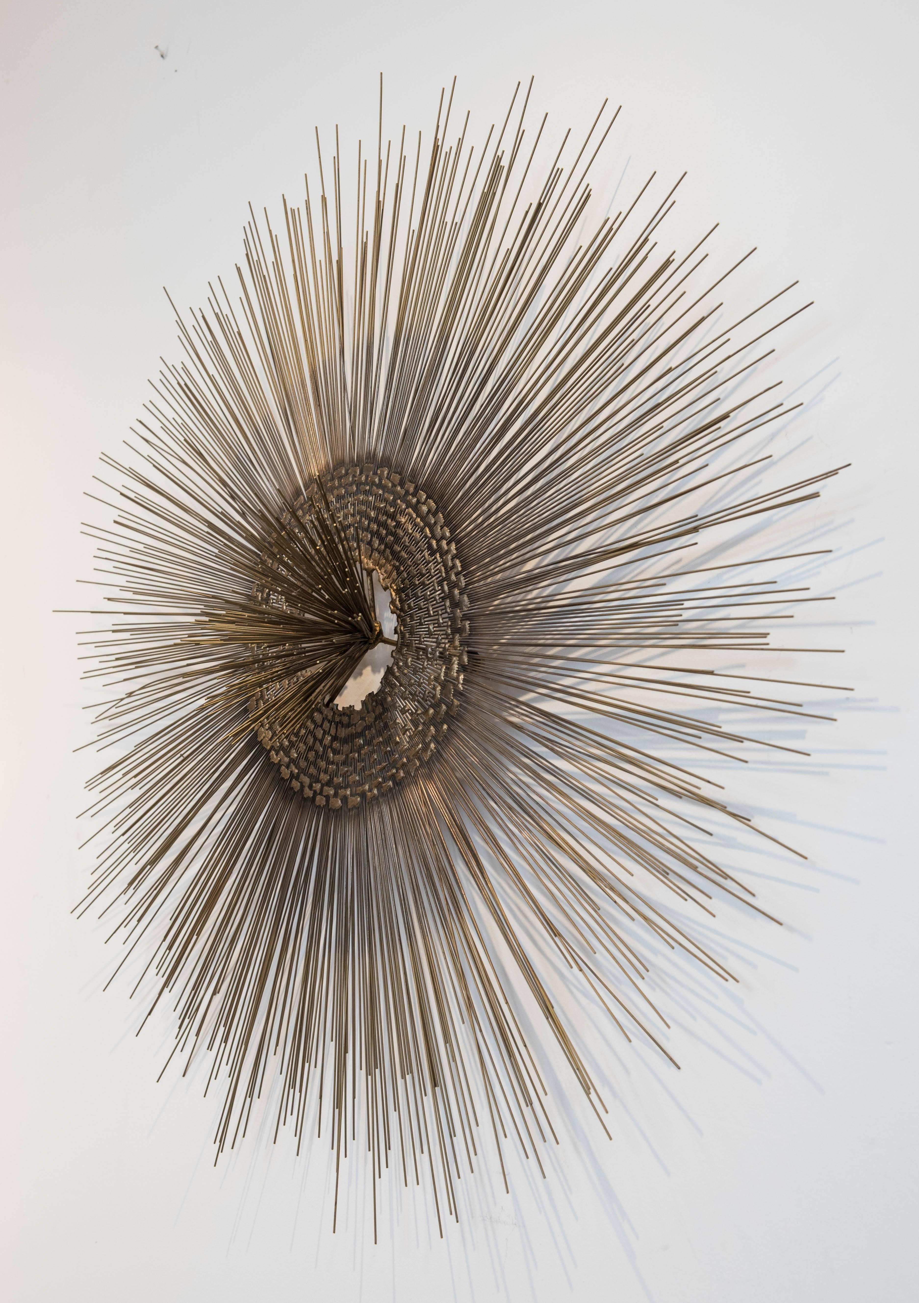 A splendid and Classic bronze-brass colored metal starburst wall sculpture with multiple metal rods surrounding a mesh interior with a metal rod 