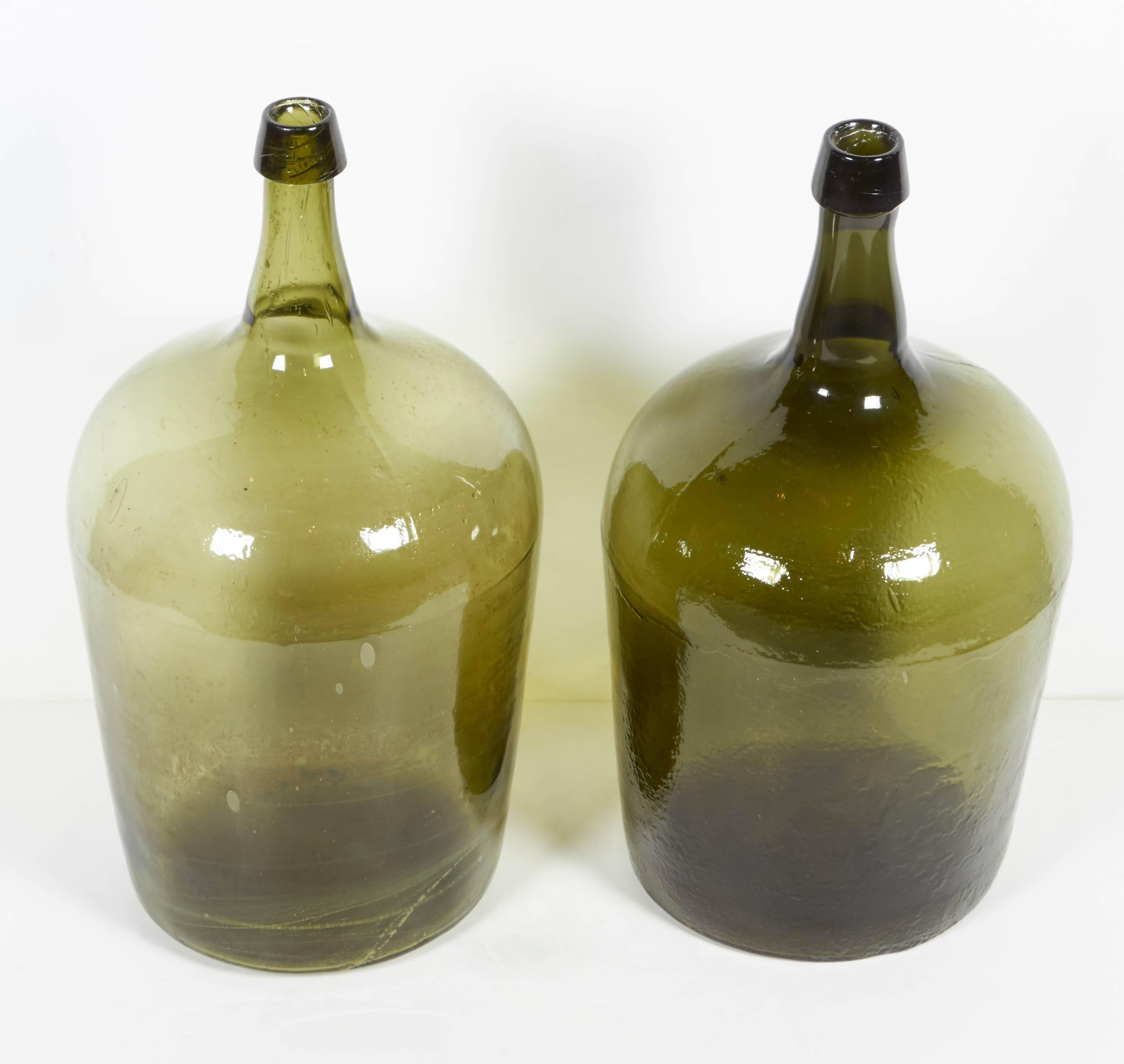 Two antique handblown glass demijohns from France with rough pontil bottoms. Each is beautifully shaped and distinctly colored, one with a wonderfully quirky tilt in the spout emphasizing it's handmade origins. 
GL218.
